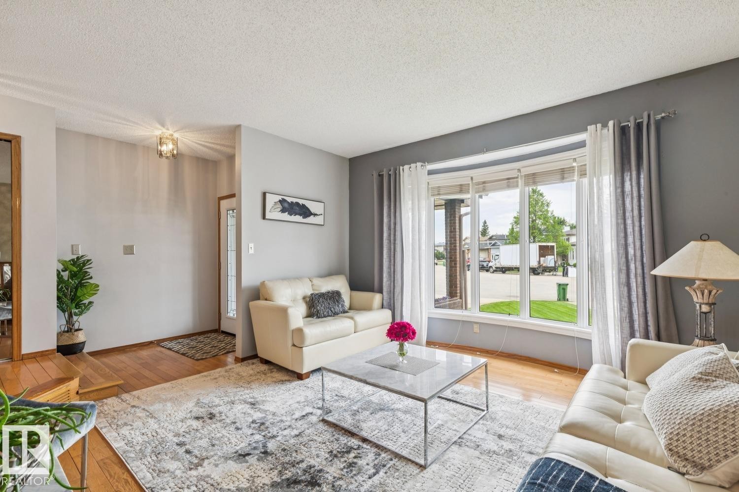 Living area featuring a large bay window, wood-finish flooring, and a decorative overhead light fixture at the entryway - 15804 80 Street, Edmonton, AB