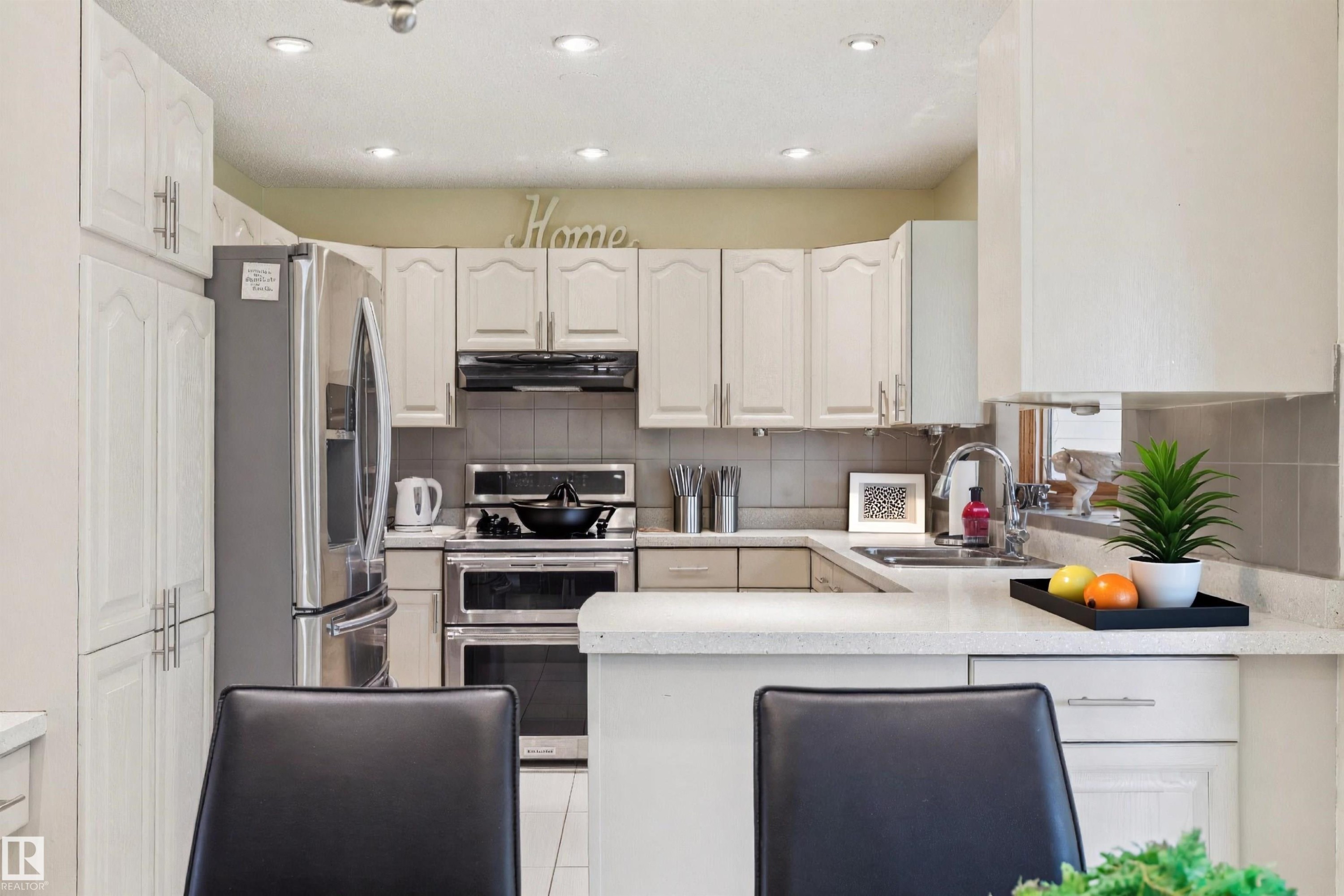 Bright kitchen featuring white cabinetry, integrated stainless steel appliances, recessed ceiling lighting, a tile backsplash, and a light-toned countertop - 15804 80 Street, Edmonton, AB