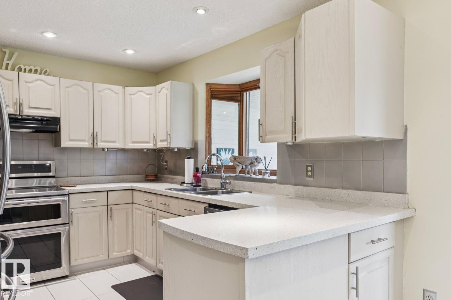 Kitchen featuring light-toned cabinetry, light-colored countertops, and stainless steel double ovens - 15804 80 Street, Edmonton, AB