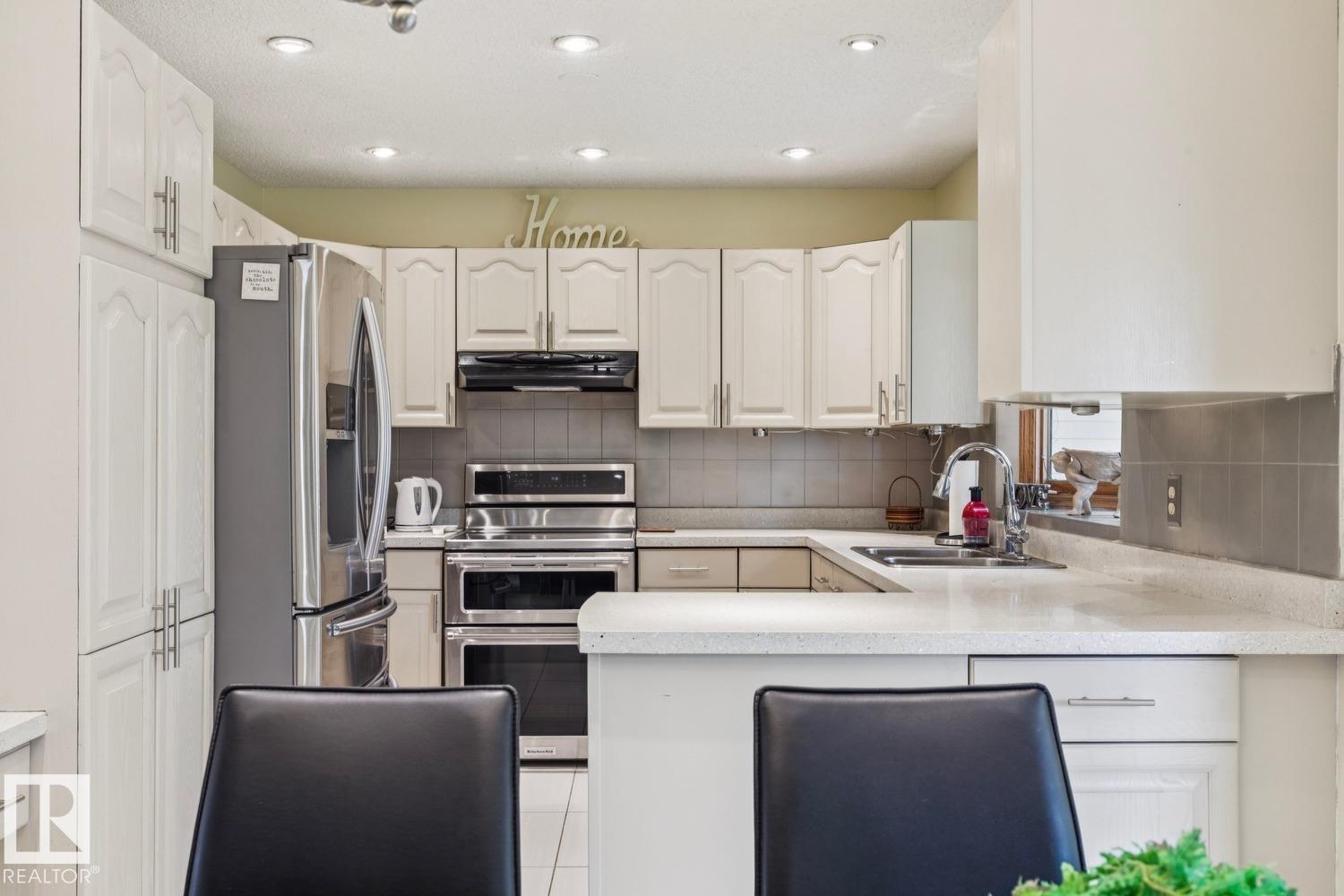 Kitchen featuring white cabinetry, stainless steel appliances, recessed lighting, a tile backsplash, and light-colored countertops - 15804 80 Street, Edmonton, AB