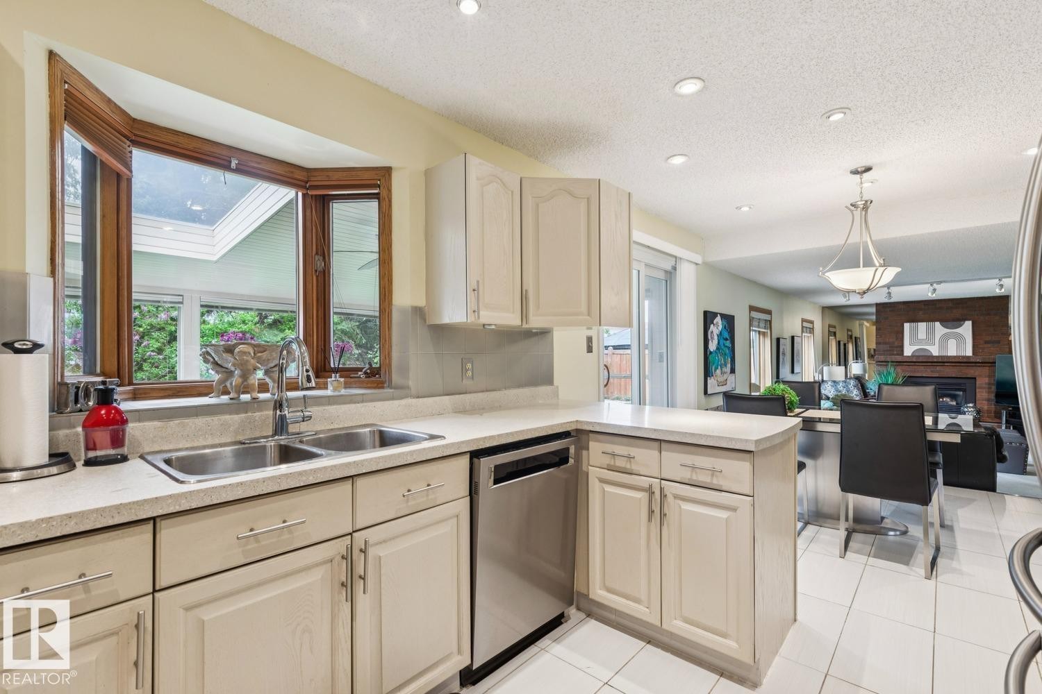 Kitchen featuring a double stainless steel sink, wood-framed bay window, light cabinetry, light countertops, and stainless steel appliances - 15804 80 Street, Edmonton, AB