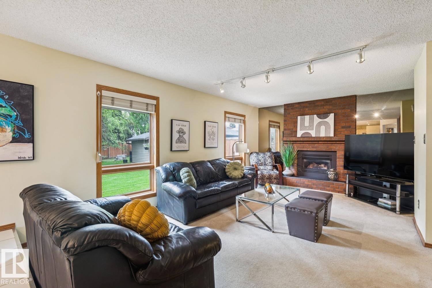 Living area featuring a brick-surround fireplace with hearth, track lighting, and windows with wood trim - 15804 80 Street, Edmonton, AB