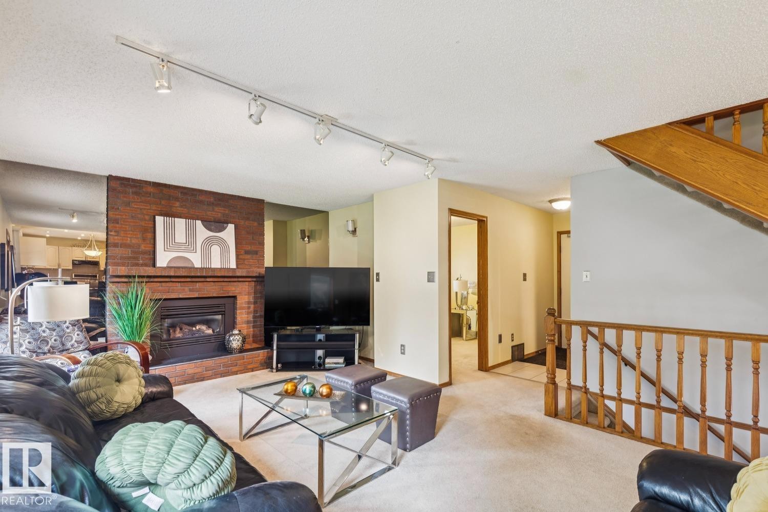 Living area featuring a brick fireplace surround with a gas insert, track lighting, and carpeted flooring - 15804 80 Street, Edmonton, AB