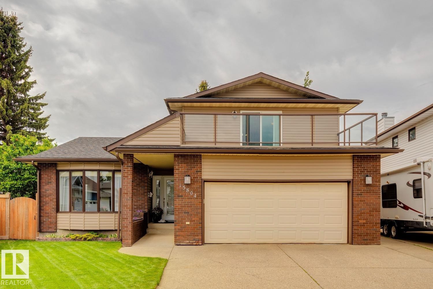 Brick and siding exterior featuring an attached two-car garage, a second-story balcony with glass railing, and a bay window - 15804 80 Street, Edmonton, AB