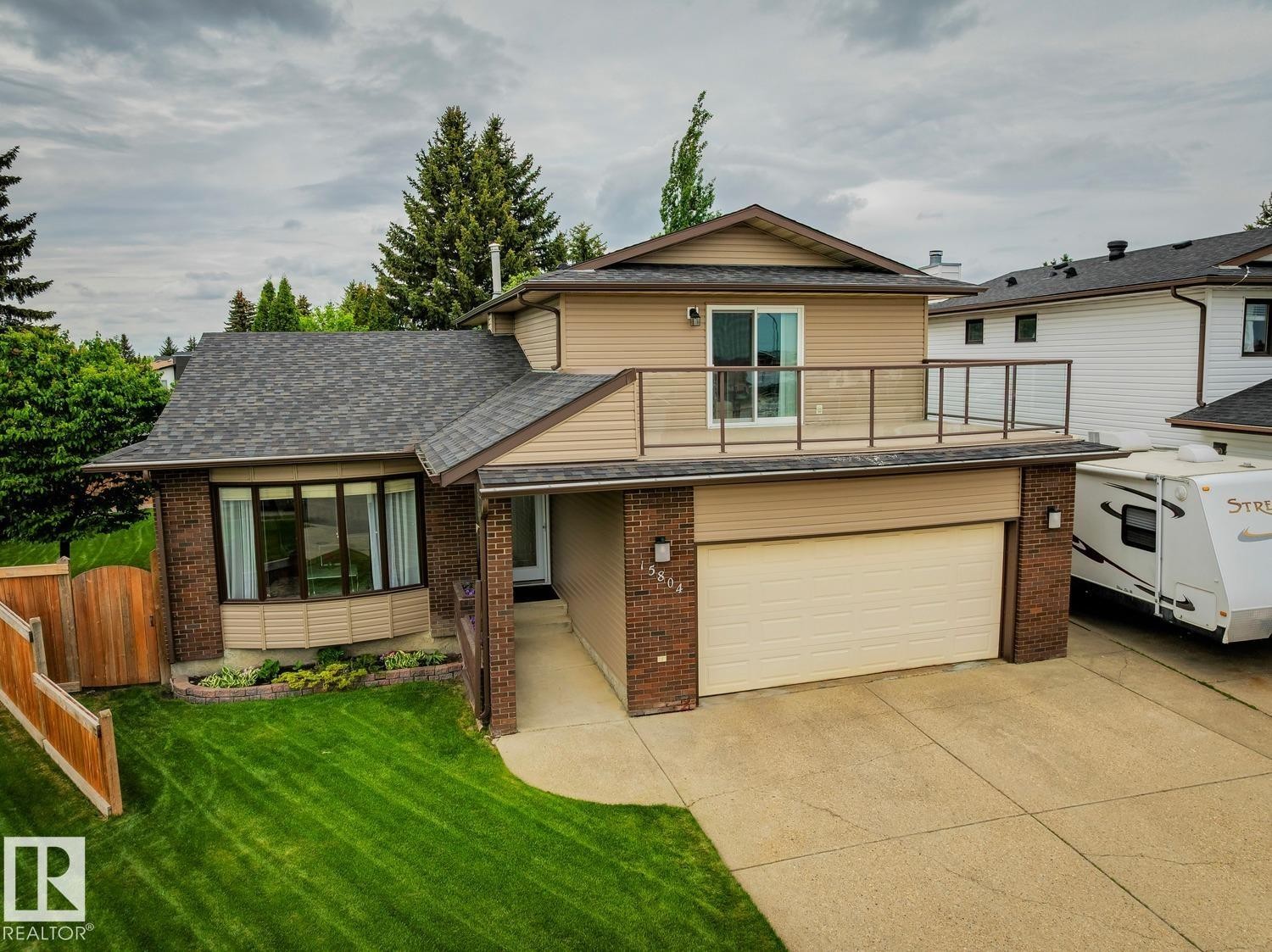 Two-story property featuring a brick and siding exterior, an attached garage, a second-story balcony with glass railing, a bay window, and a manicured lawn - 15804 80 Street, Edmonton, AB
