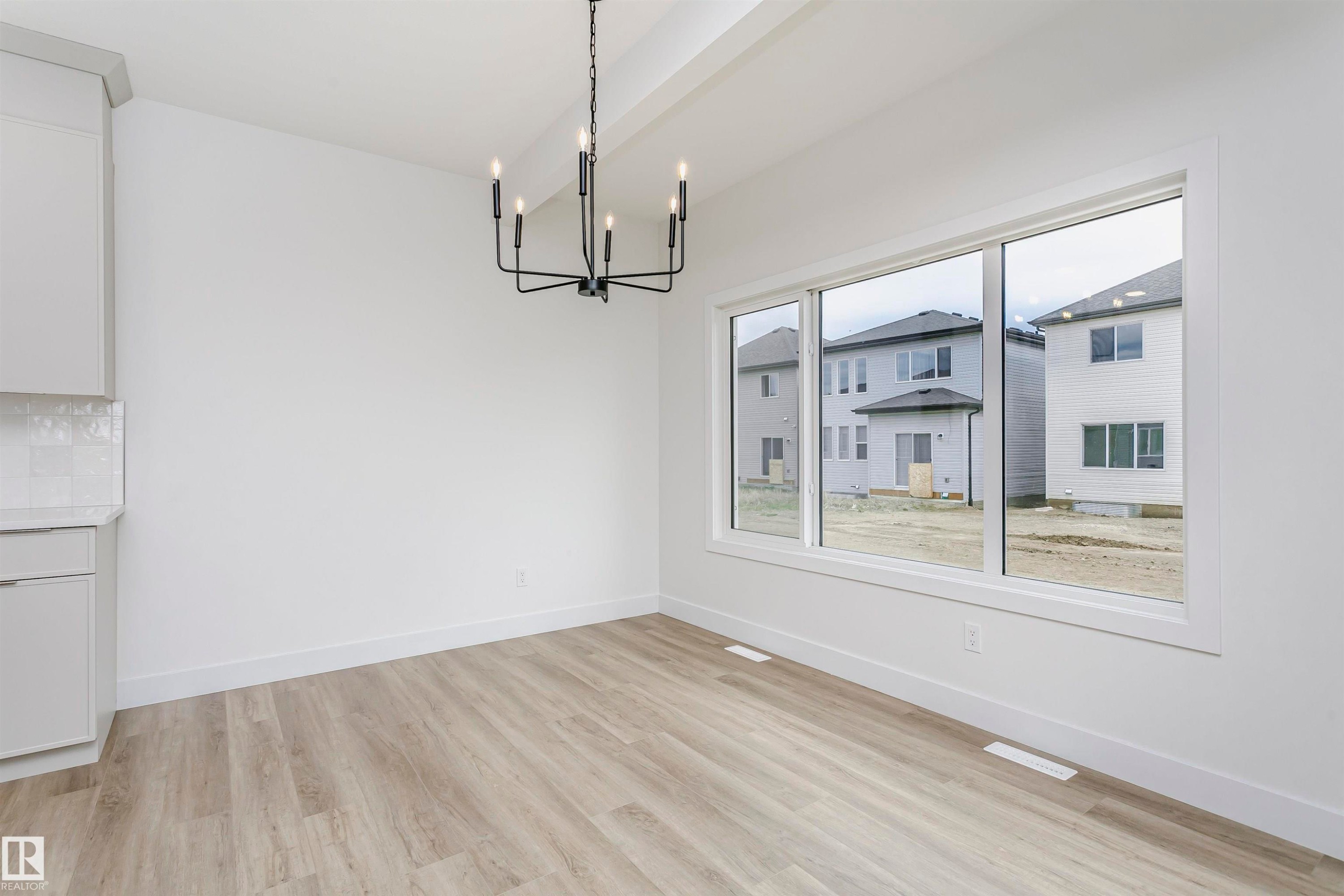 Bright interior space featuring a multi-pane window, wood-finish flooring, and a contemporary black chandelier - 6210 Dansereau Crescent, Beaumont, AB
