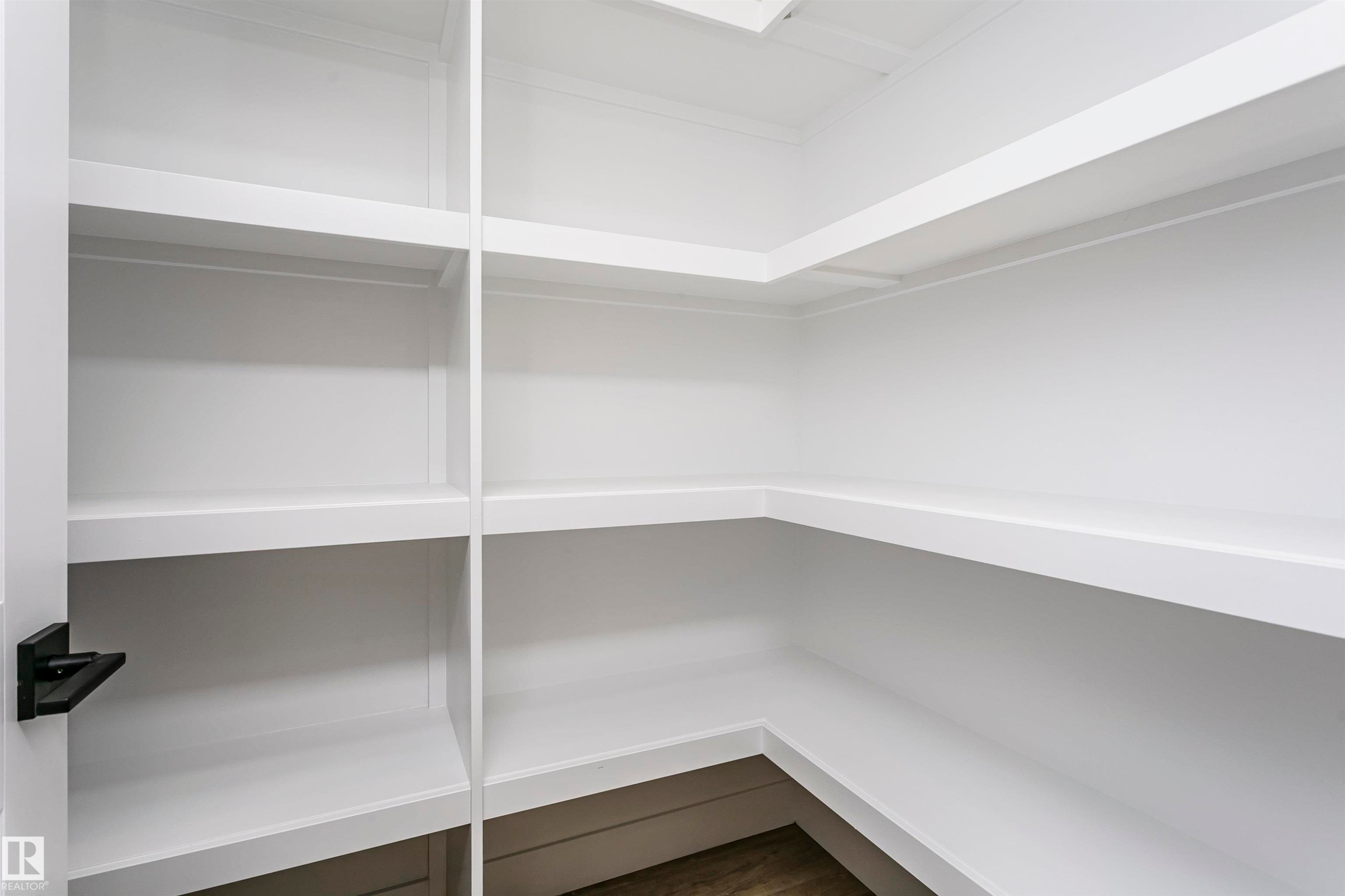 Expansive pantry featuring built-in white shelving, wood-finish flooring, and a black lever door handle - 6210 Dansereau Crescent, Beaumont, AB