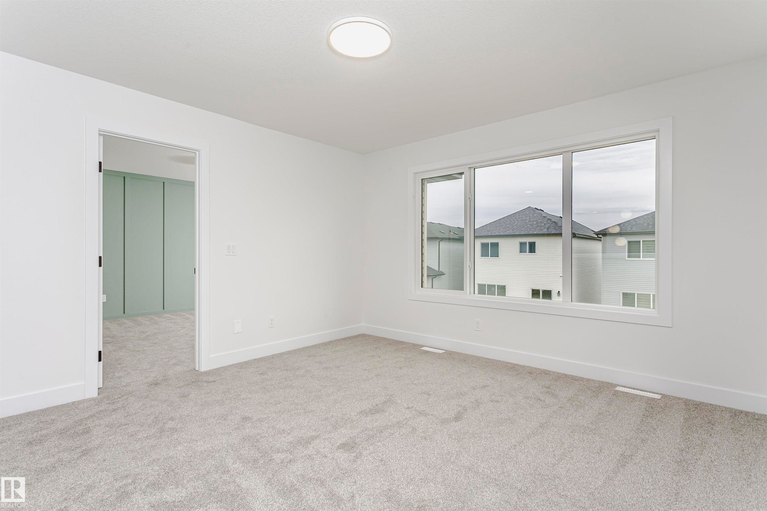 Bright interior space featuring a large three-panel window, light gray carpeting, and a flush-mount ceiling light fixture - 6210 Dansereau Crescent, Beaumont, AB