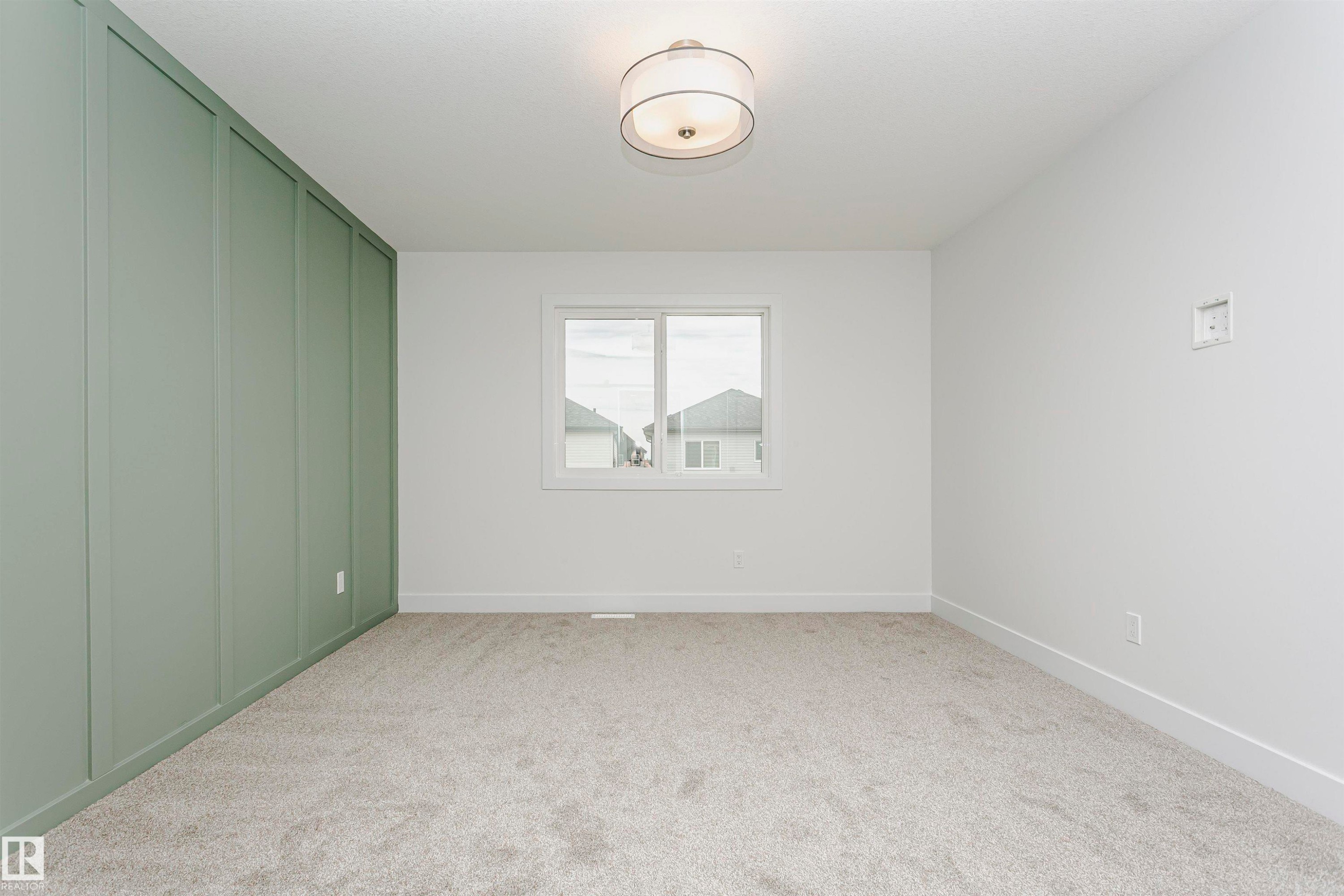 Room featuring a light green accent wall with vertical paneling, white walls, and light gray carpeted flooring - 6210 Dansereau Crescent, Beaumont, AB