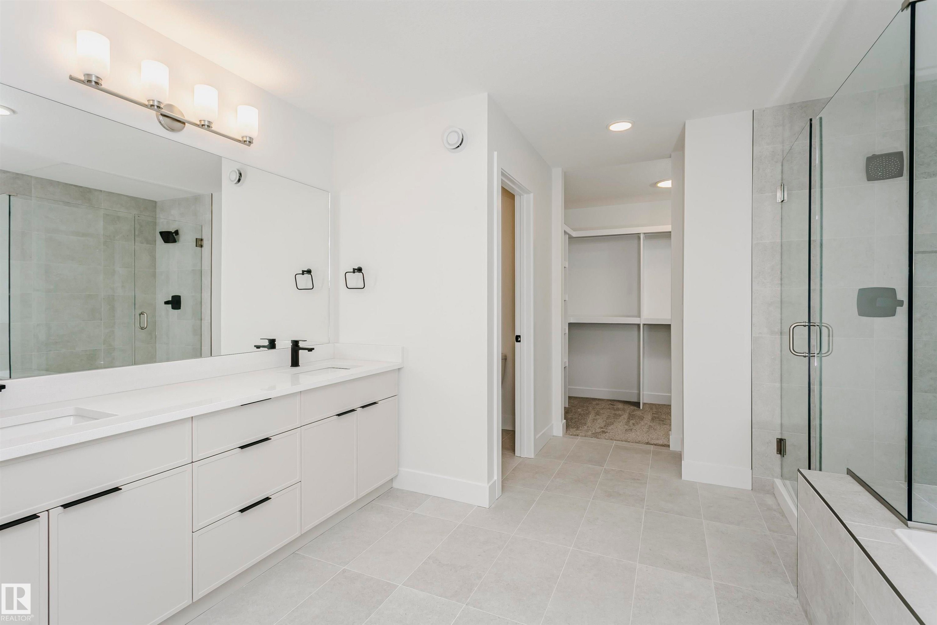 Spacious bathroom featuring a dual vanity with white cabinetry, quartz countertops, and matte black fixtures - 6210 Dansereau Crescent, Beaumont, AB