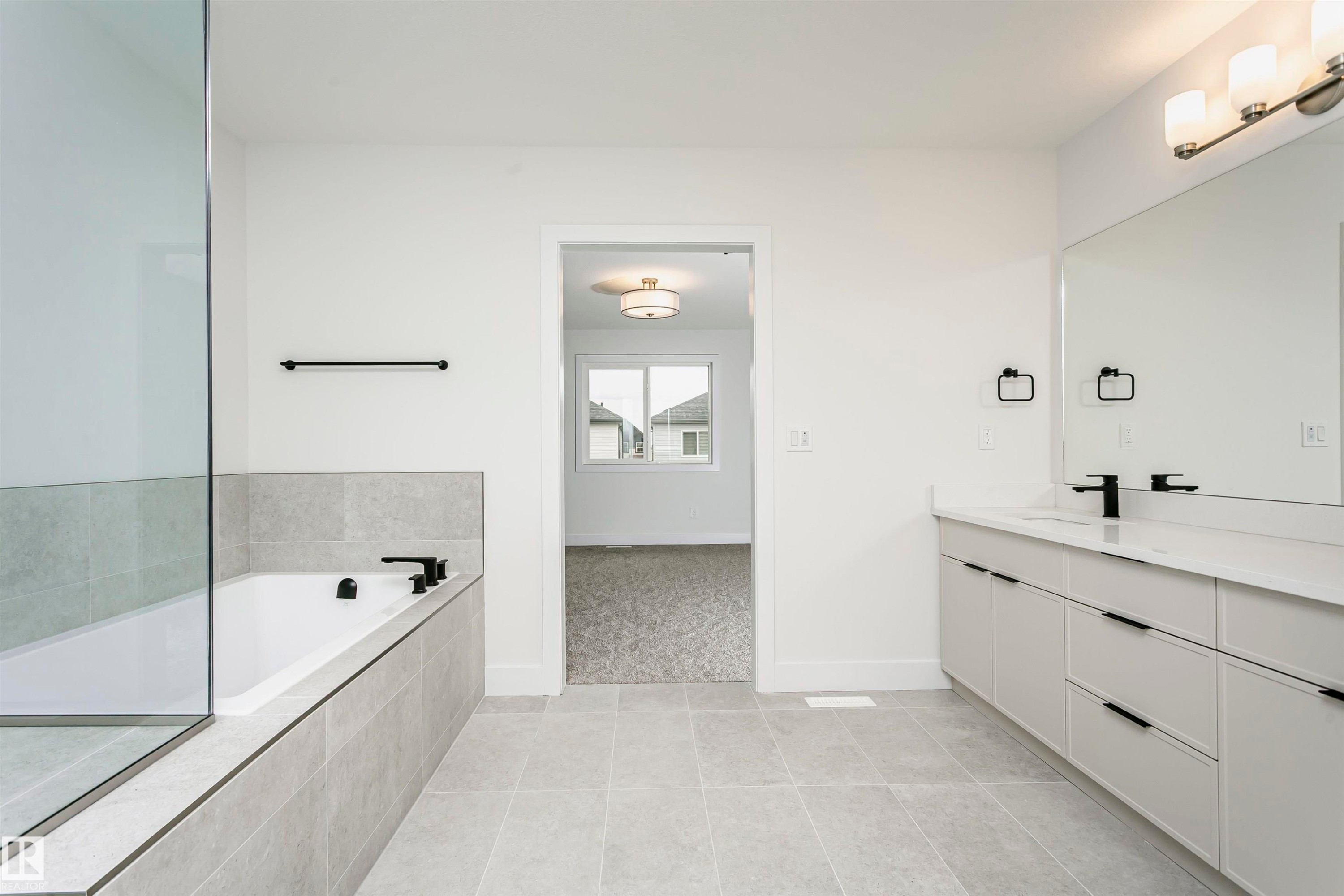 Spacious bathroom featuring a dual vanity with a large mirror, a built-in bathtub with tiled surround, a separate glass-enclosed shower, and large format tile flooring - 6210 Dansereau Crescent, Beaumont, AB