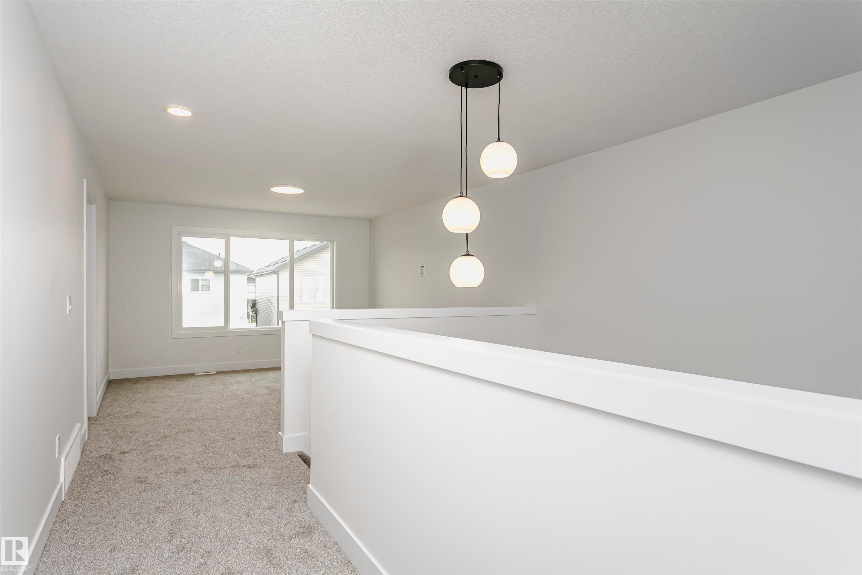 Bright upper landing featuring a contemporary three-globe pendant light, recessed lighting, white wall and trim finishes, gray carpet, and large windows - 6210 Dansereau Crescent, Beaumont, AB