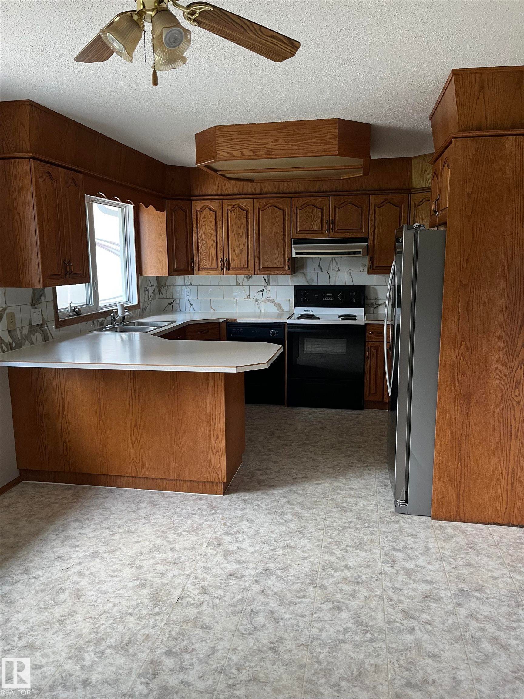 Kitchen featuring wood cabinetry, white countertops, black appliances, a double basin sink, and a ceiling fan - 5012 58 Avenue, Viking, AB - Indoor Photo Showing Kitchen