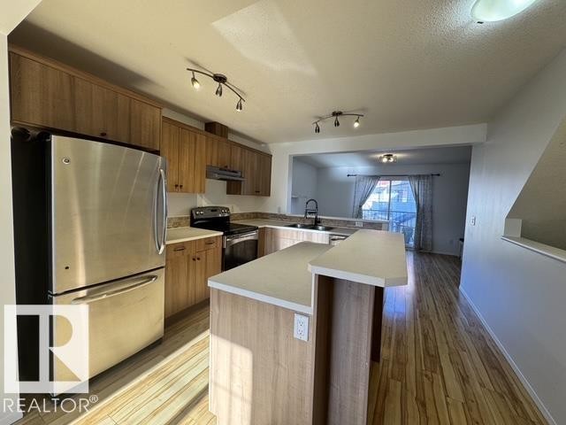Kitchen featuring stainless steel appliances, wood-finish cabinetry, light-toned countertops, and wood-finish flooring - #13 3751 12 Street, Edmonton, AB