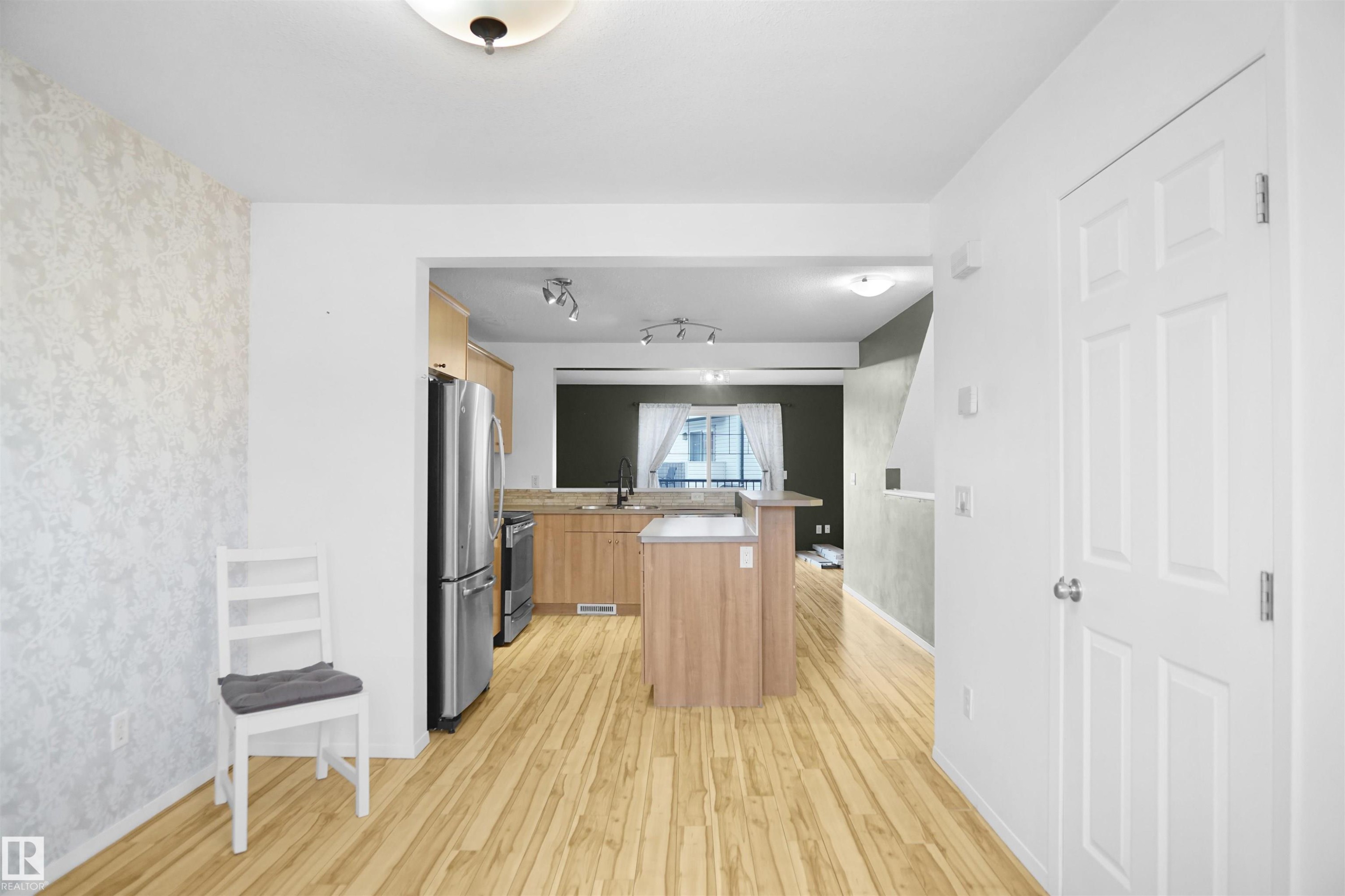 The kitchen features a central island, stainless steel appliances, and wood cabinetry - #13 3751 12 Street, Edmonton, AB