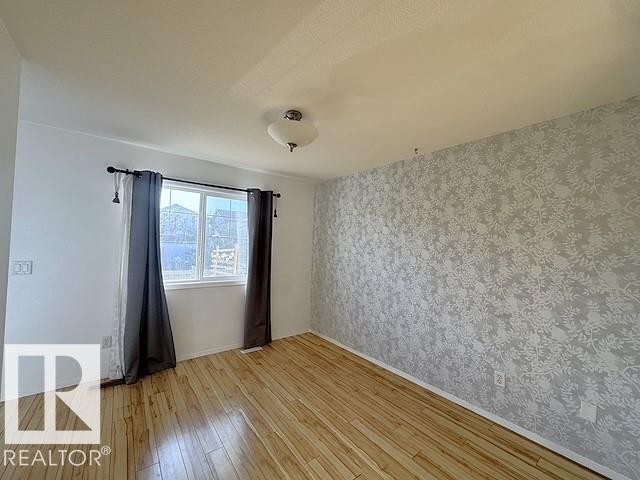 Room featuring wood-finish flooring, a decorative accent wall with a floral pattern, and a ceiling-mounted light fixture - #13 3751 12 Street, Edmonton, AB