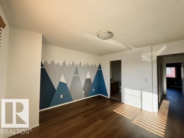 Room featuring a mountain-themed accent wall, wood-finish flooring, and white baseboards - #13 3751 12 Street, Edmonton, AB