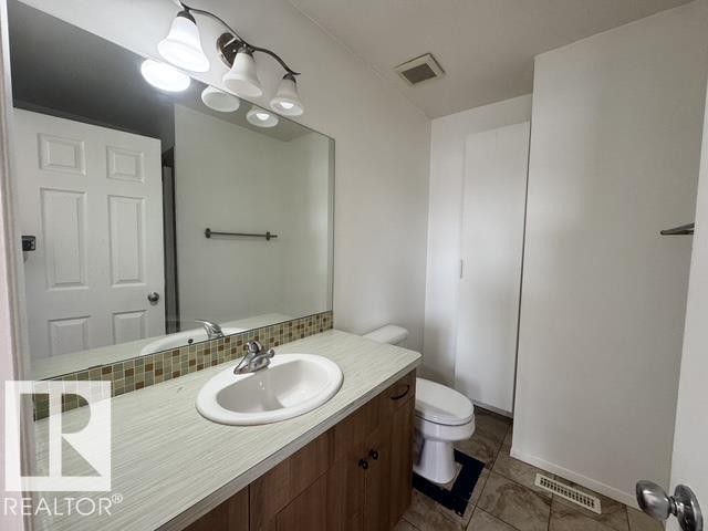 Bathroom featuring a vanity with an integrated sink, laminate countertop, and wood-finish cabinetry - #13 3751 12 Street, Edmonton, AB