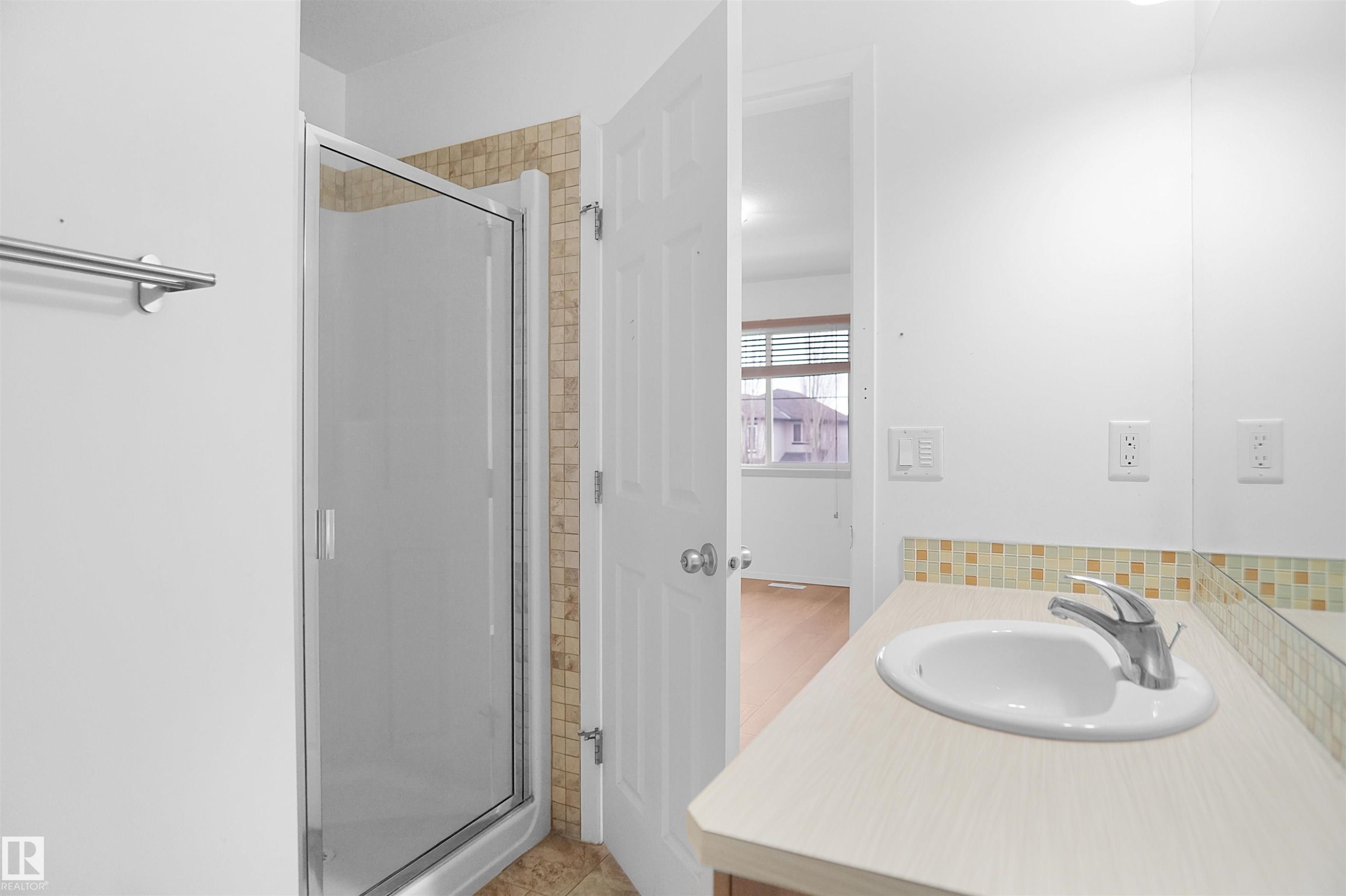 The bathroom features a shower with a clear glass enclosure and tiled surround, a vanity with an integrated sink, a chrome faucet, and a tiled backsplash - #13 3751 12 Street, Edmonton, AB