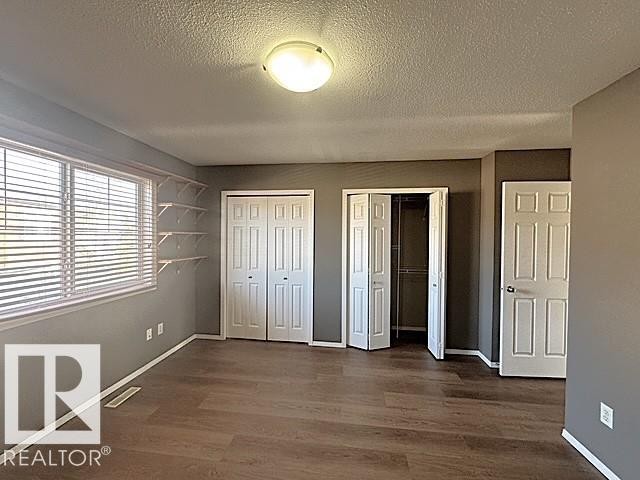 Spacious room featuring wood-finish flooring, multiple paneled doors, and a large window with horizontal blinds - #13 3751 12 Street, Edmonton, AB