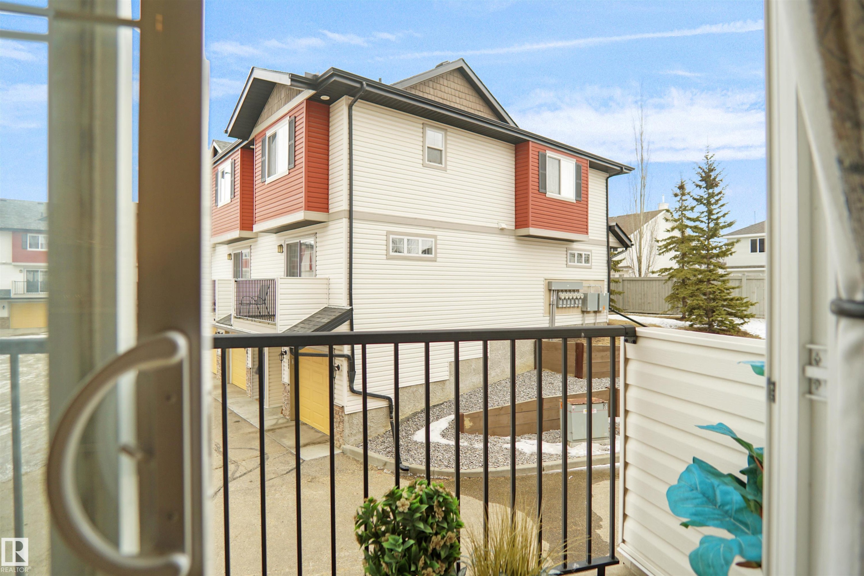 This property features durable vinyl siding, a private balcony with black railings, and an exterior highlighted by a combination of white and red paneling - #13 3751 12 Street, Edmonton, AB