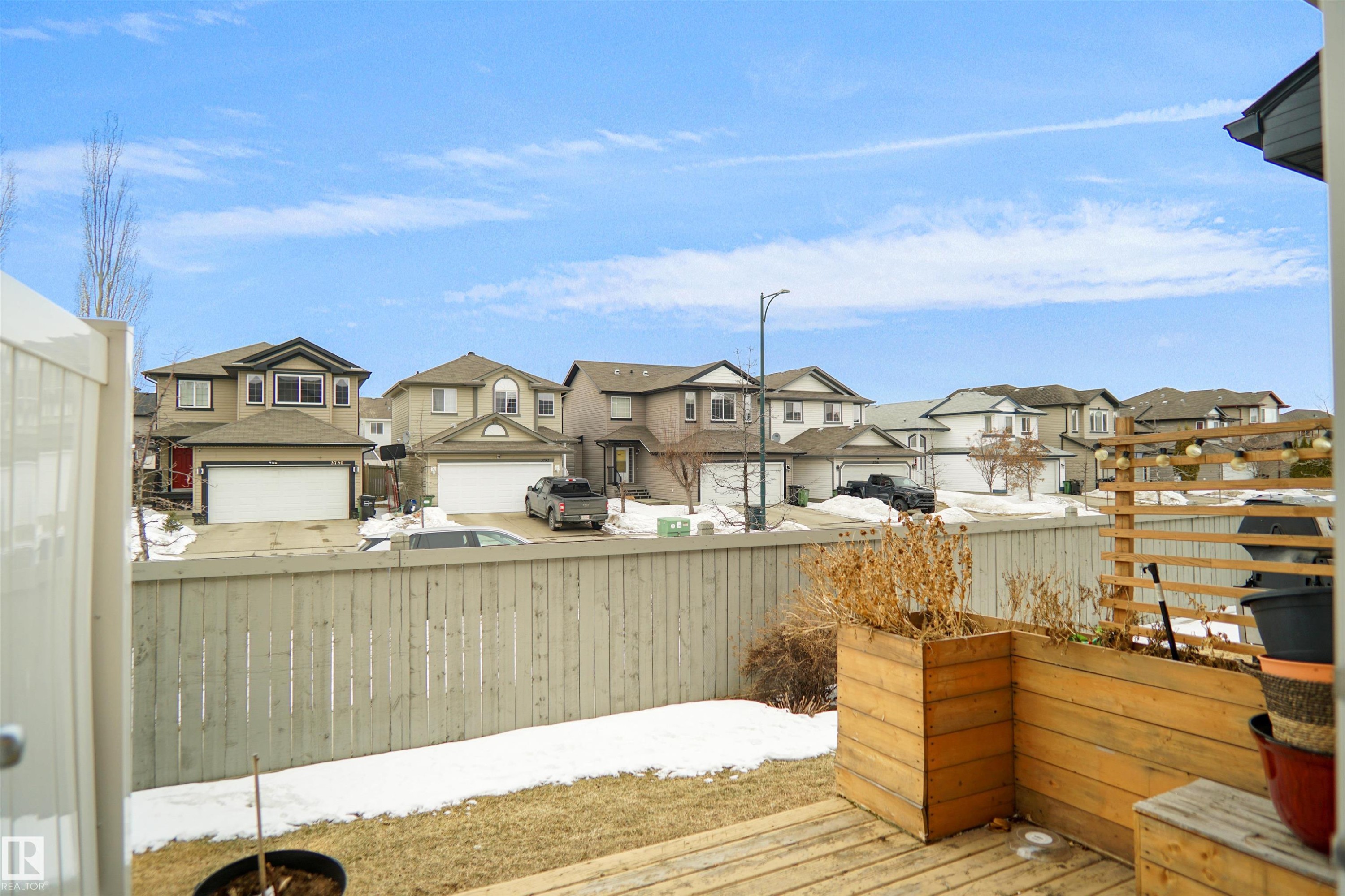 The property features a wooden deck with planter boxes, a wooden fence, and a view of residential homes - #13 3751 12 Street, Edmonton, AB