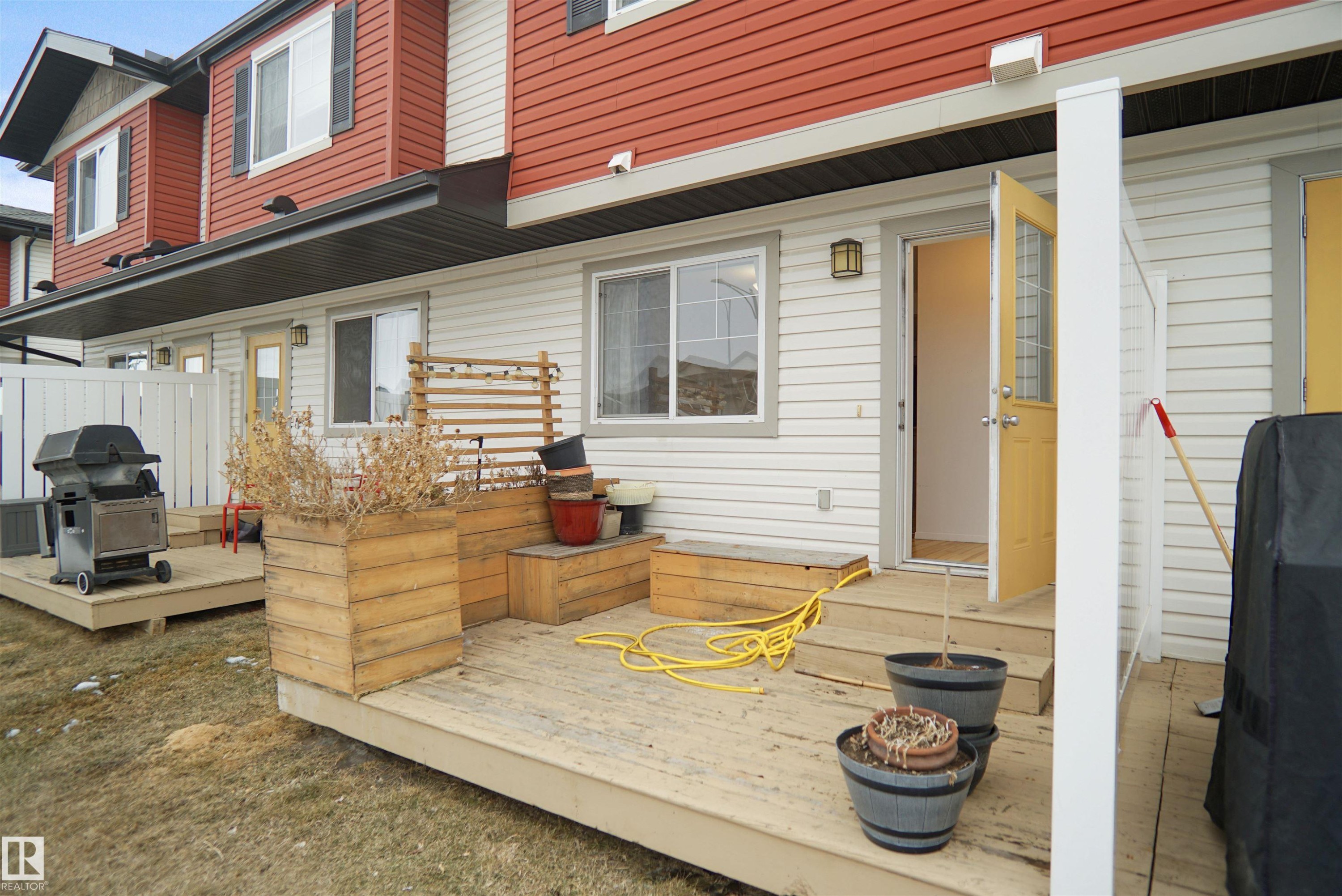 Rear exterior with a wooden deck, a wooden planter box, and a yellow door with glass panels - #13 3751 12 Street, Edmonton, AB