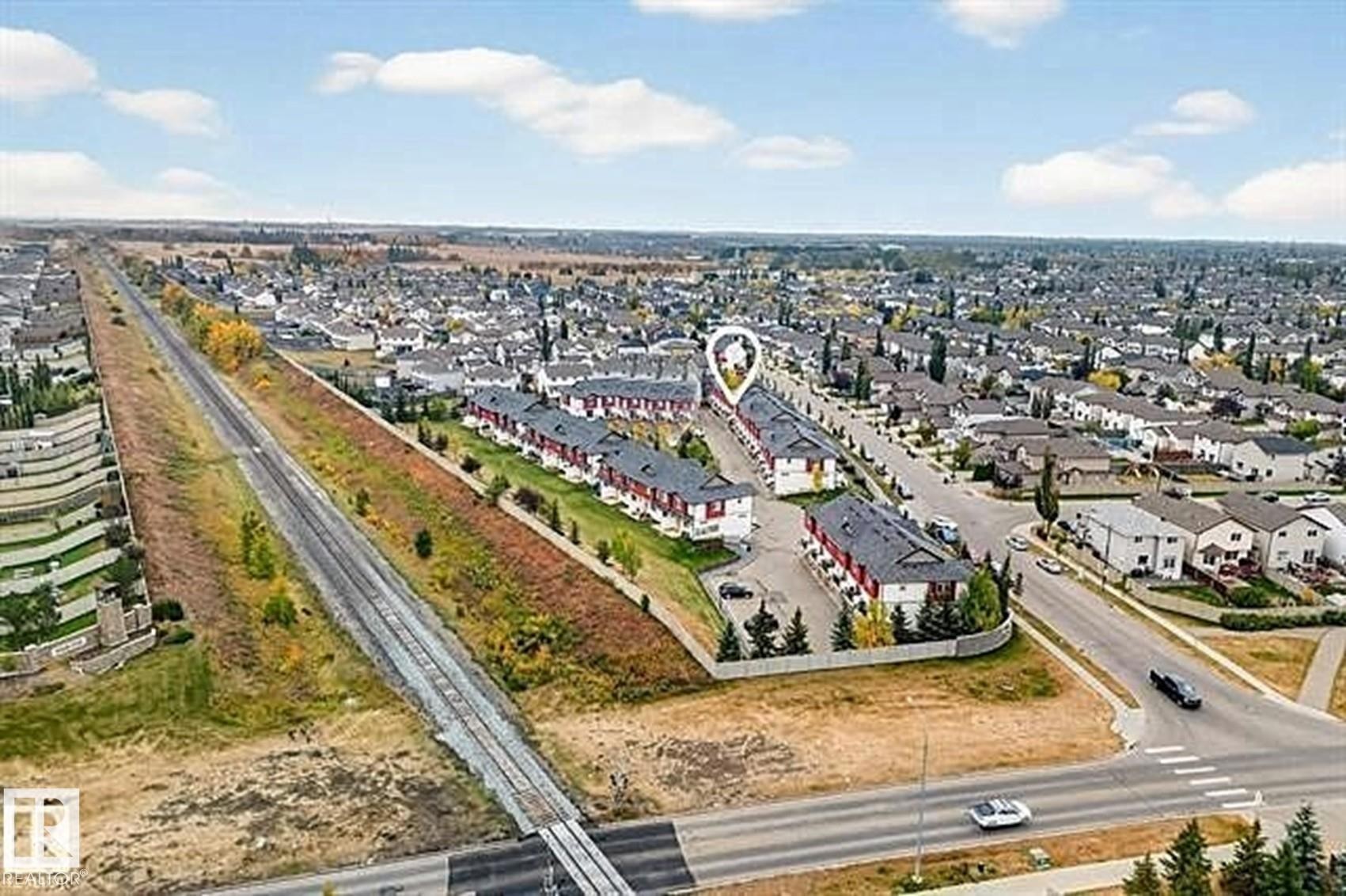 Aerial view of the property and surrounding neighborhood, featuring residential homes with dark roofs and light exteriors, and a road with crosswalk markings - #13 3751 12 Street, Edmonton, AB