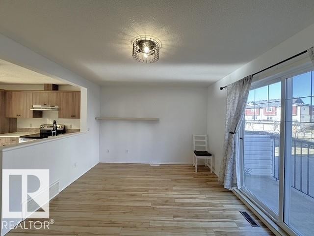 Open-concept living area featuring wood-finish flooring, a contemporary wire cage flush mount light fixture, and a sliding glass door providing abundant natural light - #13 3751 12 Street, Edmonton, AB