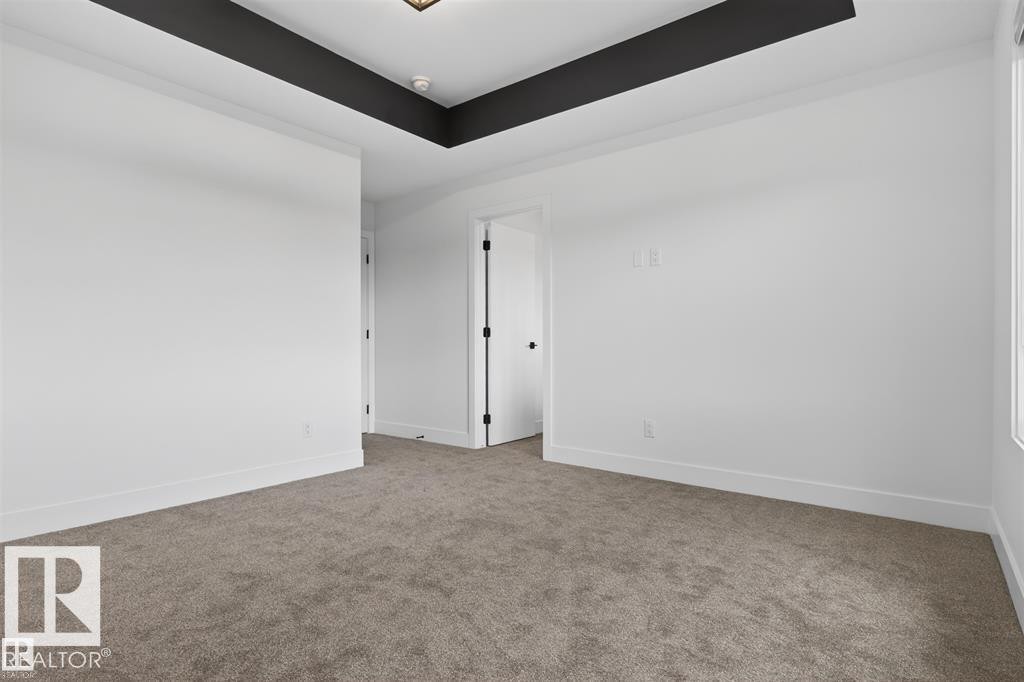 Spacious interior room featuring a tray ceiling with dark accent, light-colored walls, neutral carpeting, and white trim - 41 River Birch Way, St. Albert, AB