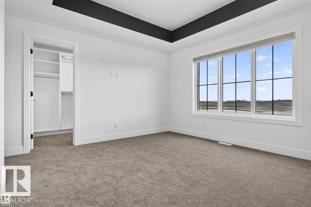 Spacious room with a large multi-pane window, neutral-toned carpet, and a custom tray ceiling - 41 River Birch Way, St. Albert, AB