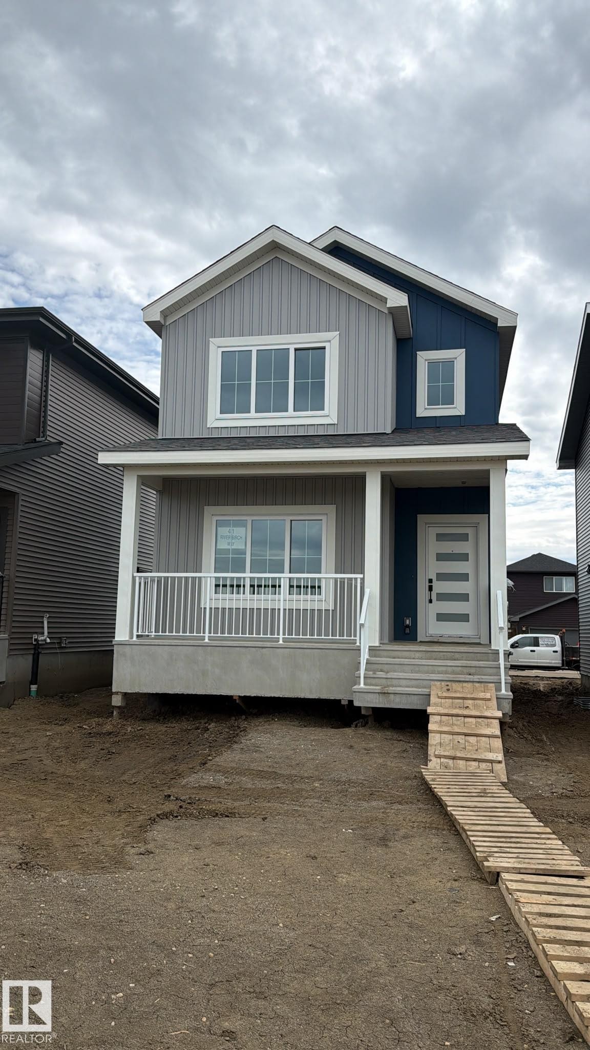 Two-story home featuring a covered front porch with white railing, vertical siding in contrasting gray and blue tones, white trim, and a contemporary front door with horizontal glass inserts - 41 River Birch Way, St. Albert, AB