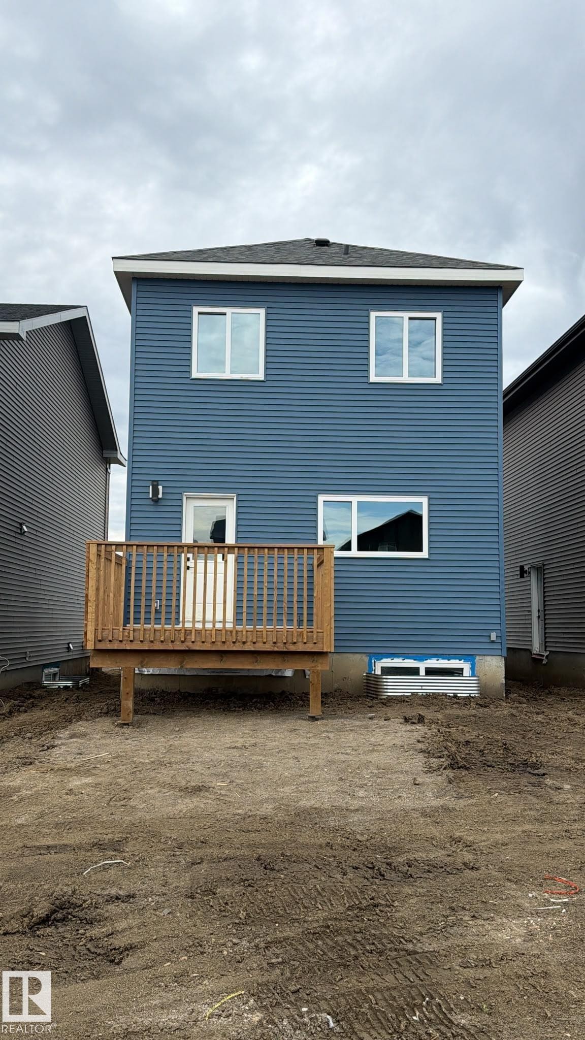 Rear exterior featuring blue horizontal siding, white trim, a dark asphalt shingle roof, a wooden deck, and white framed windows - 41 River Birch Way, St. Albert, AB