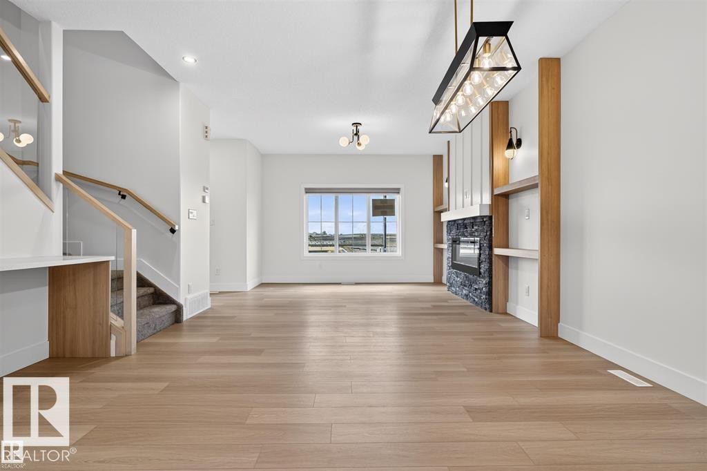 Expansive living space featuring light wood-finish flooring, a modern linear fireplace with dark stone surround, and built-in shelving with wood accents - 41 River Birch Way, St. Albert, AB