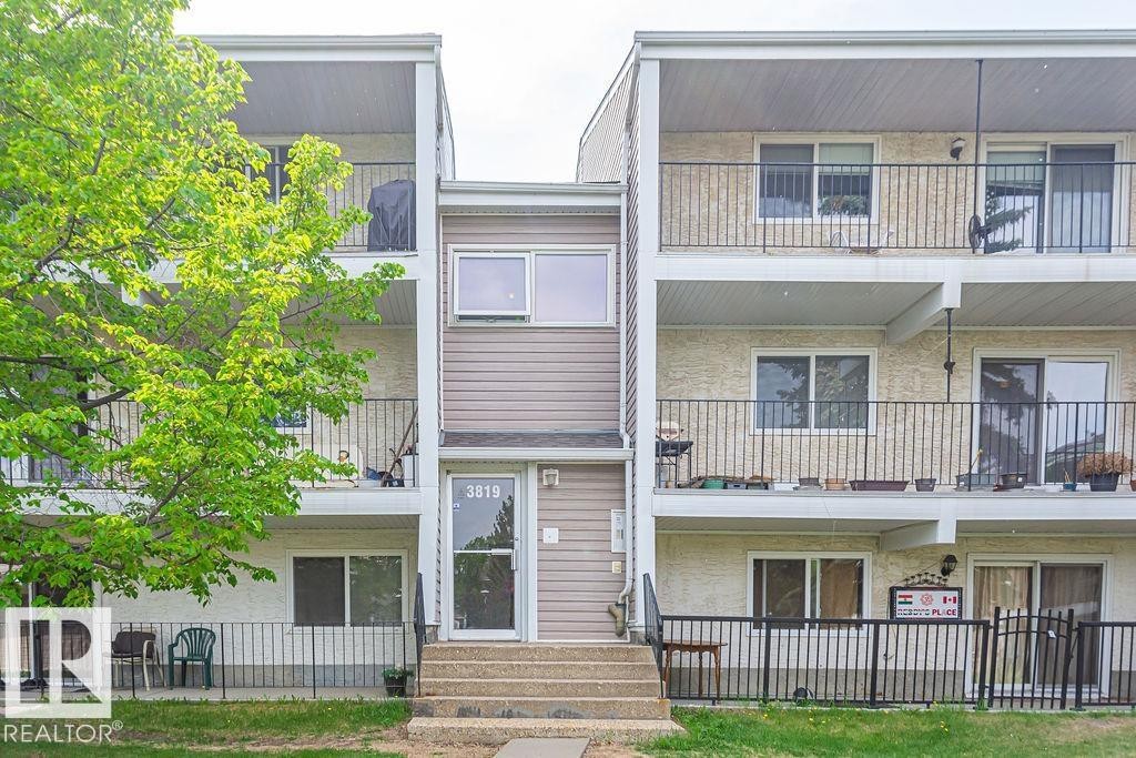 Multi-level residential building featuring private balconies with black metal railings, a stucco exterior, and a central entrance with exterior stairs - 6 3819 76 Street, Edmonton, AB