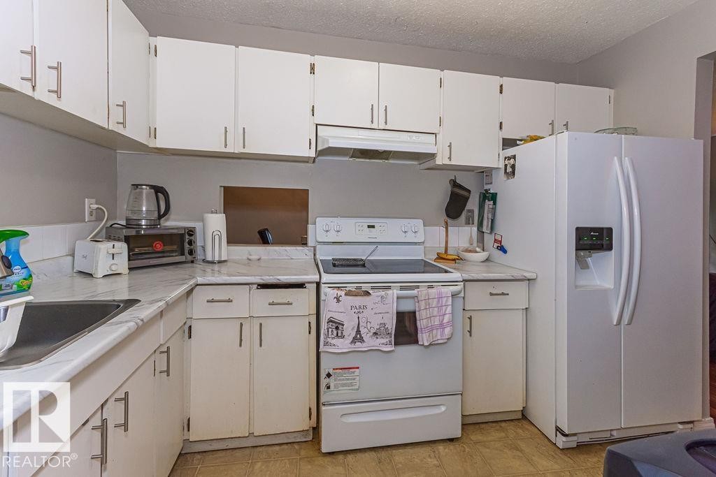 Functional kitchen featuring white cabinetry, white appliances, corner sink, and marble-look countertops - 6 3819 76 Street, Edmonton, AB