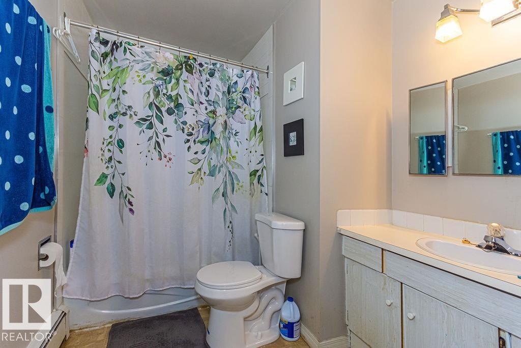 Full bathroom featuring a white vanity with integrated sink, two wall-mounted mirrored medicine cabinets, an overhead light fixture, and a toilet - 6 3819 76 Street, Edmonton, AB