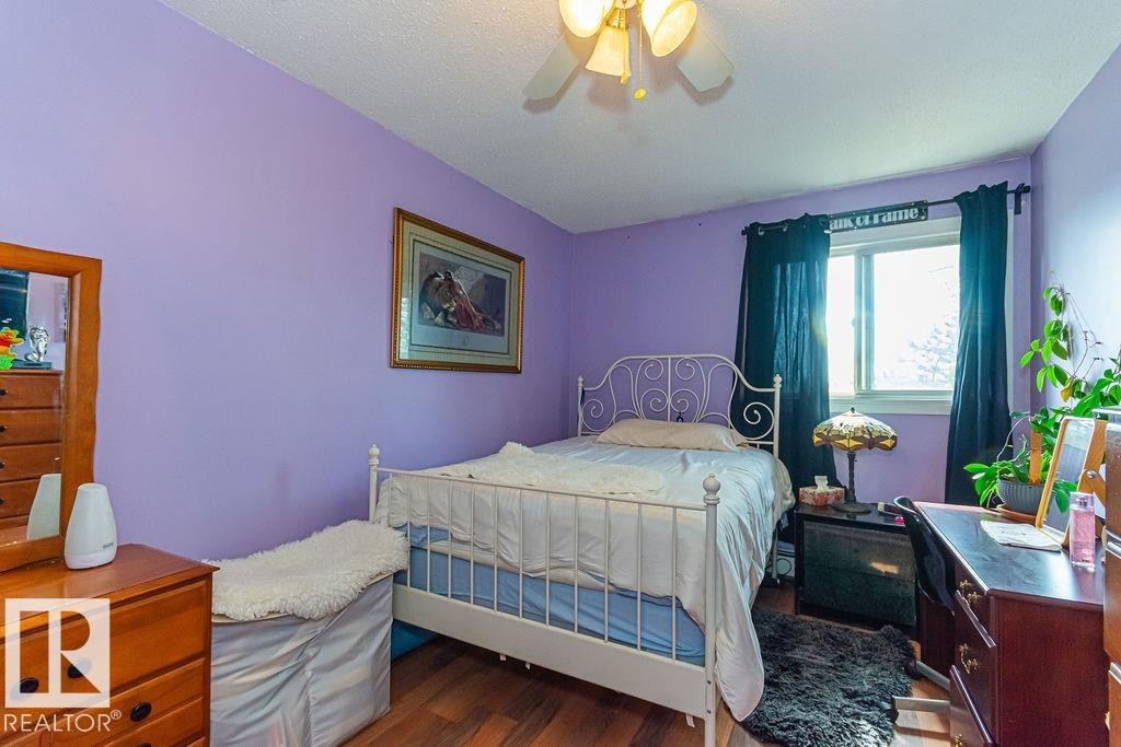 Bedroom featuring wood-finish flooring, a ceiling fan with integrated lighting, and a single window with dark drapery - 6 3819 76 Street, Edmonton, AB
