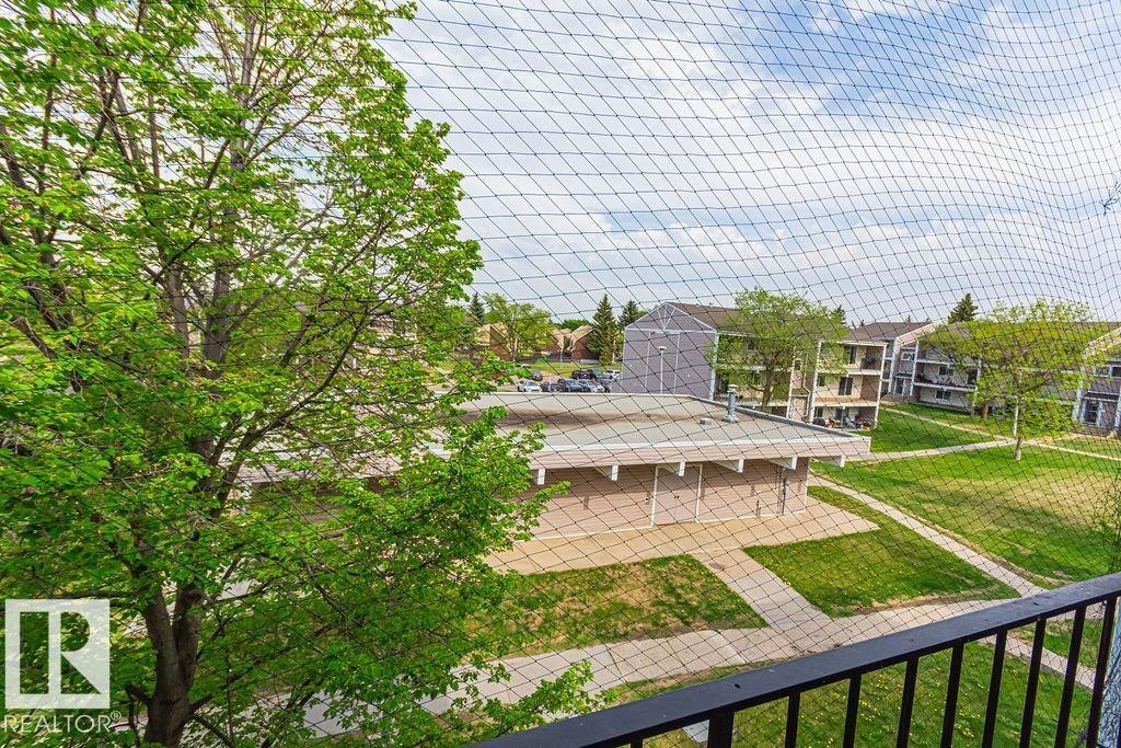 Balcony featuring a black metal railing and expansive views of the surrounding green spaces and building exteriors - 6 3819 76 Street, Edmonton, AB