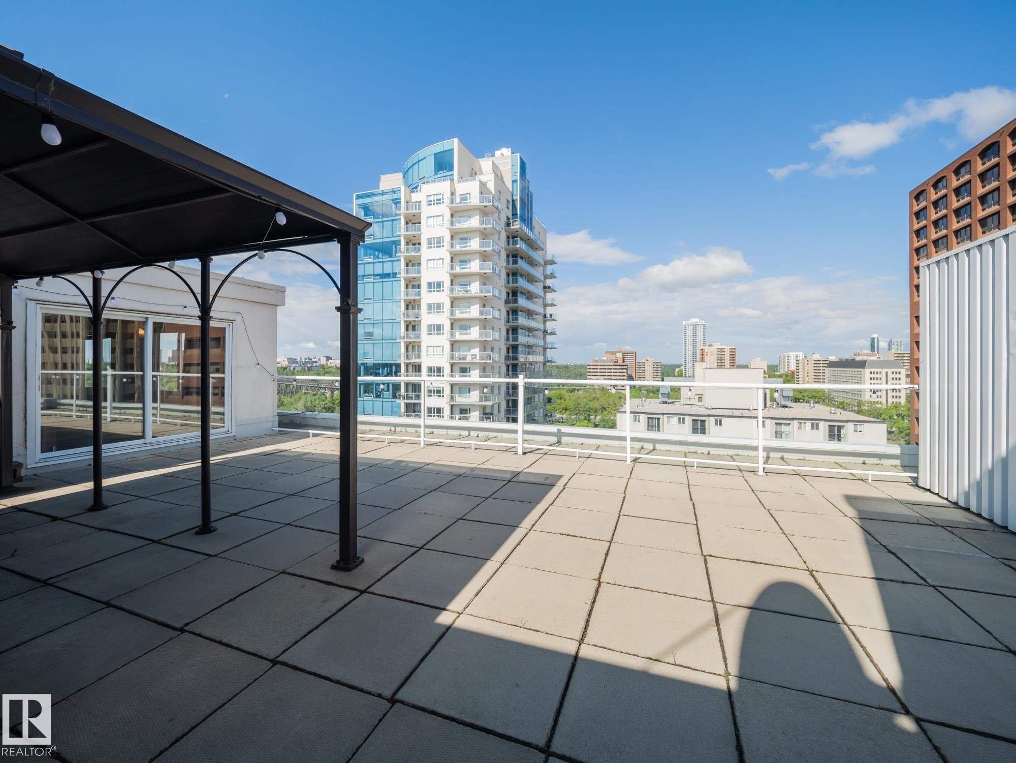 Expansive rooftop patio featuring large format pavers, a white metal railing, and a black metal gazebo frame - #Ph4 9725 106 St Nw, Edmonton, AB - Outdoor