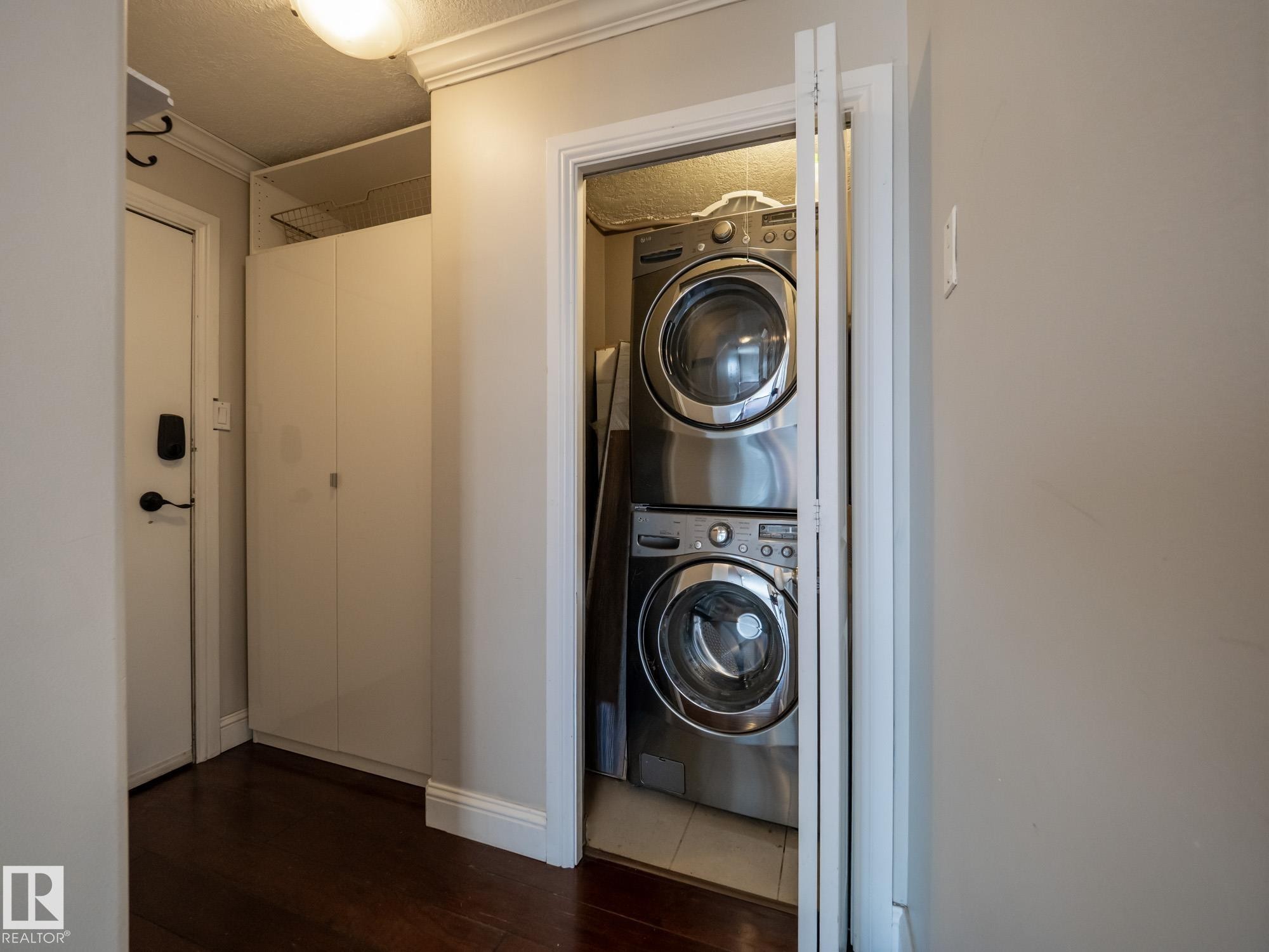 Integrated laundry closet featuring stacked stainless steel front-load appliances and bifold doors - #Ph4 9725 106 St Nw, Edmonton, AB - Indoor Photo Showing Laundry Room