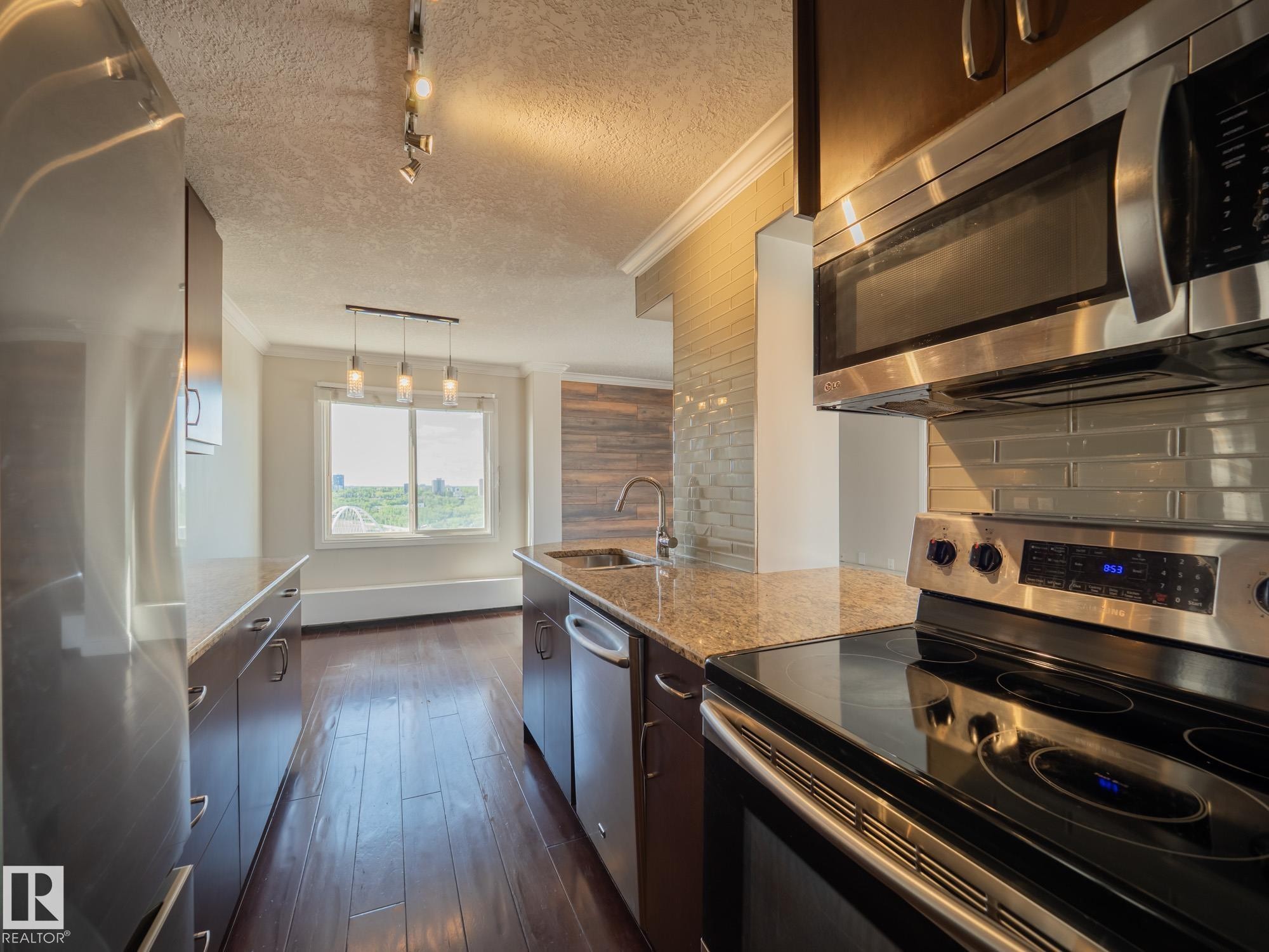 Kitchen featuring stainless steel appliances, wood-finish flooring, granite countertops, an undermount sink, and a subway tile backsplash - #Ph4 9725 106 St Nw, Edmonton, AB - Indoor Photo Showing Kitchen With Stainless Steel Kitchen