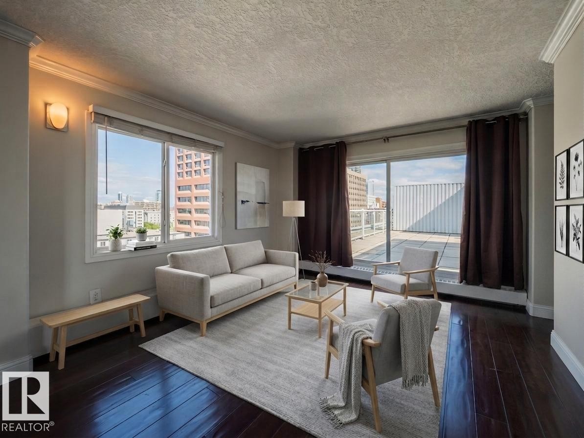Spacious living area featuring rich wood-finish flooring, crown molding, and an outdoor terrace with a tiled surface - #Ph4 9725 106 St Nw, Edmonton, AB - Indoor Photo Showing Living Room