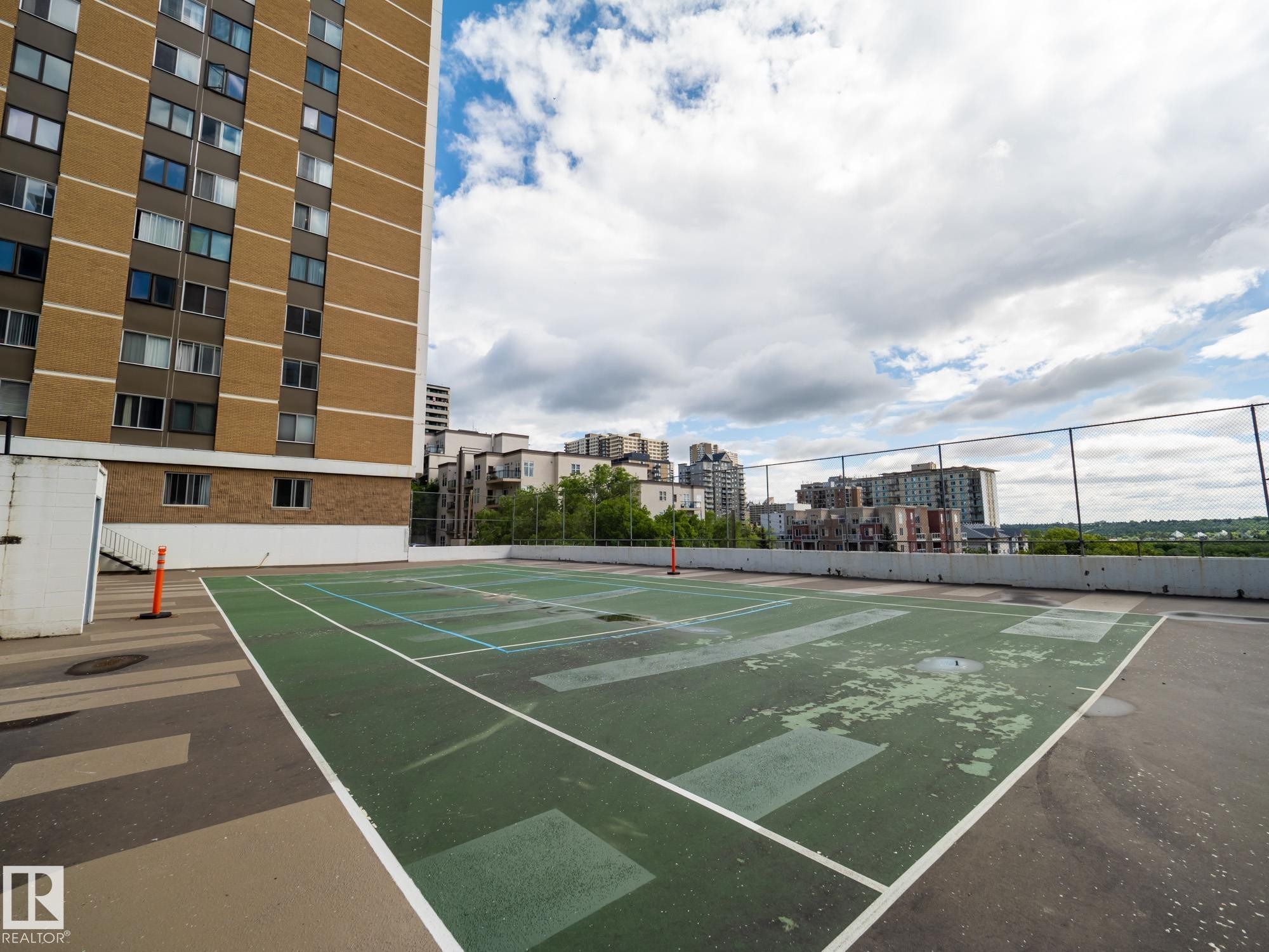 Rooftop tennis court with perimeter fencing, featuring a concrete surface and a partial building facade - #Ph4 9725 106 St Nw, Edmonton, AB - Outdoor