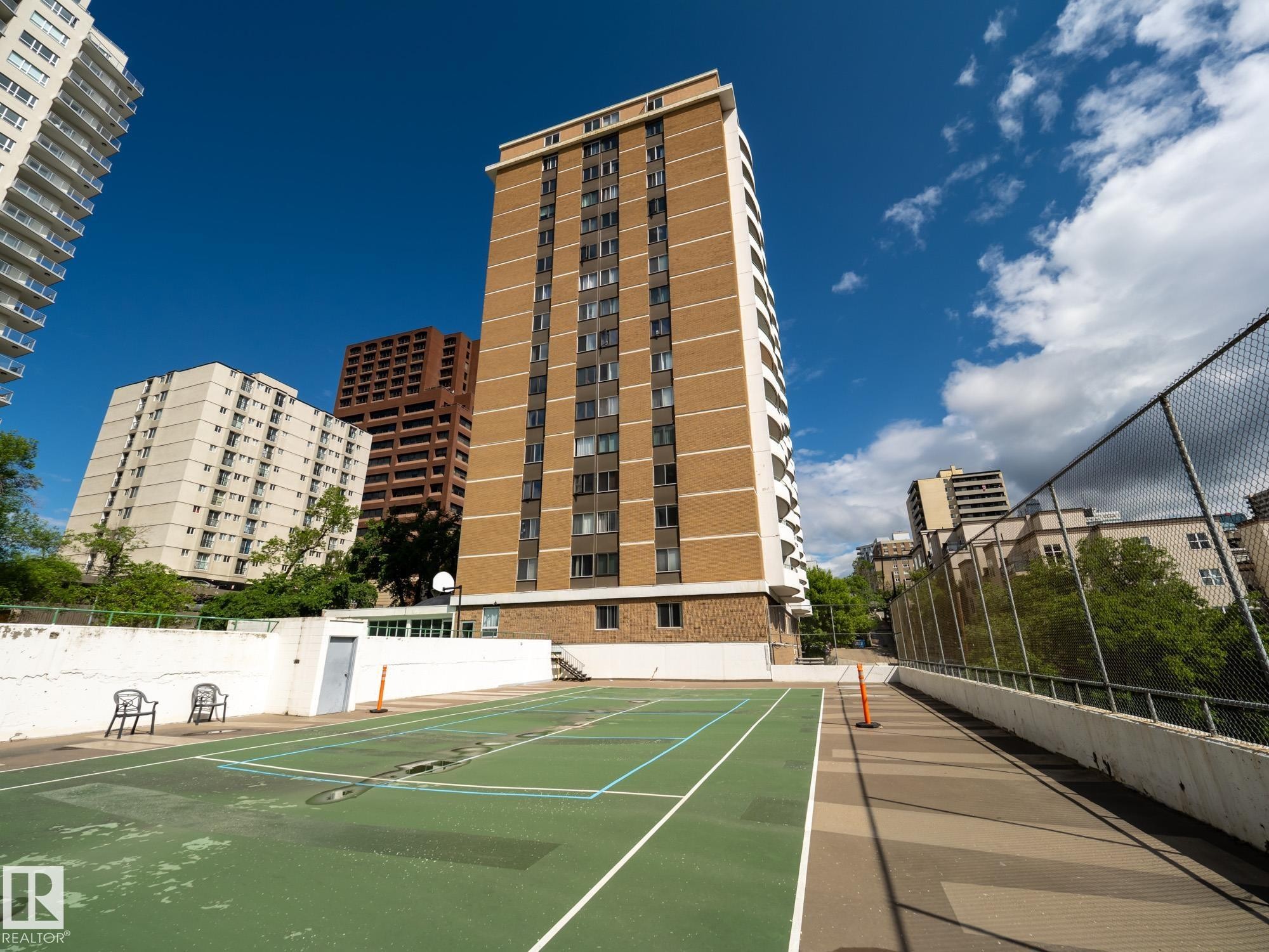 Exterior view of a high-rise building featuring brick and light-colored siding, multiple windows, and a paved walkway - #Ph4 9725 106 St Nw, Edmonton, AB - Outdoor With Facade