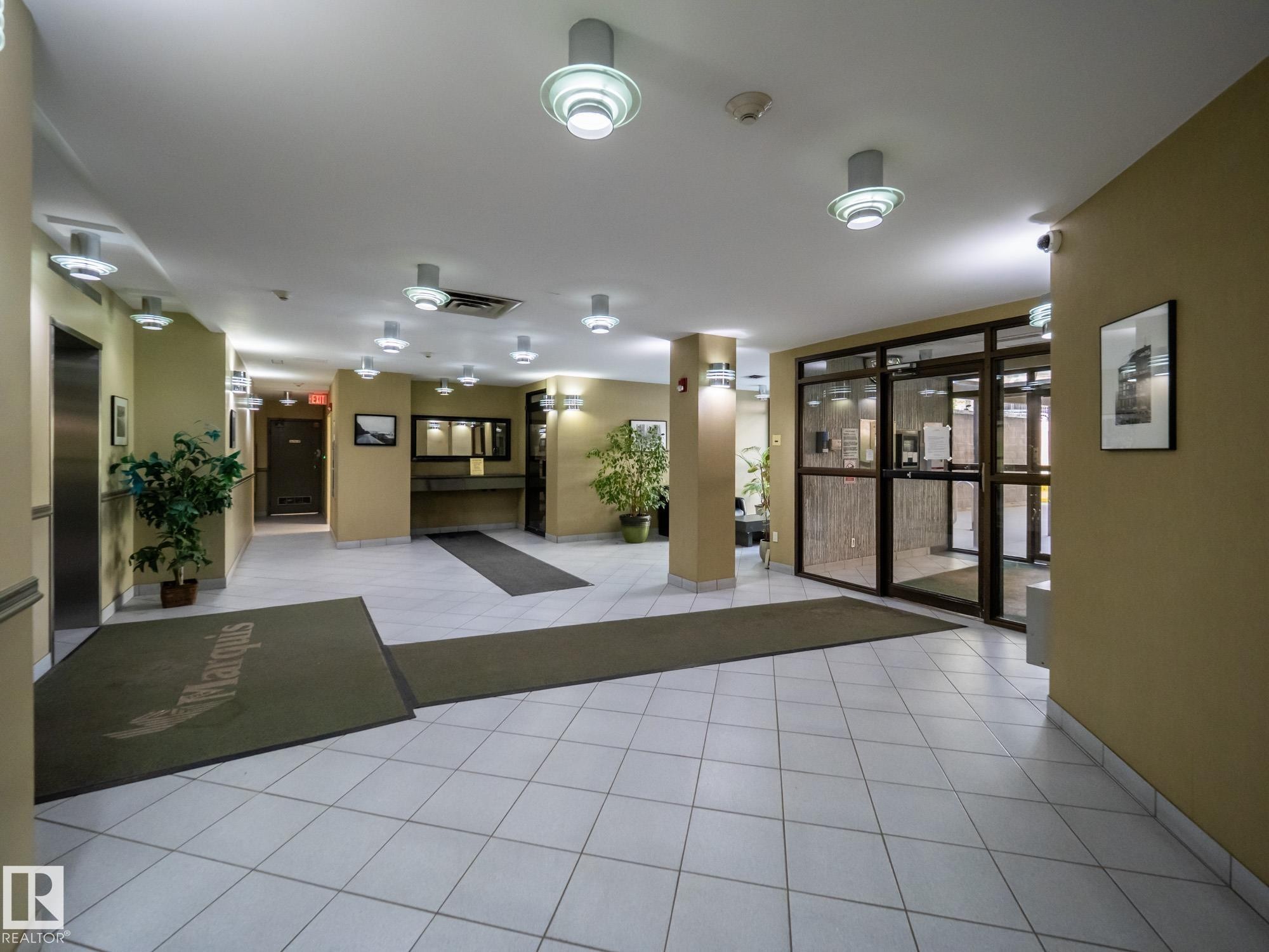 Lobby featuring white square tile flooring, recessed and wall-mounted lighting, and an elevator bank with a stainless steel door - #Ph4 9725 106 St Nw, Edmonton, AB - Indoor Photo Showing Other Room