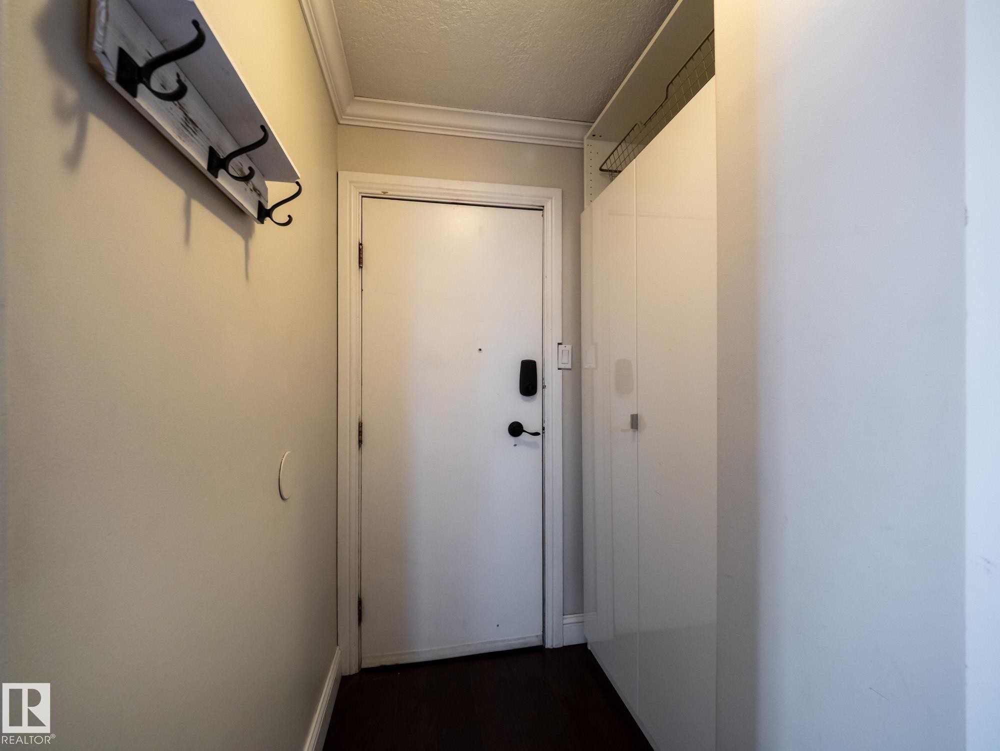 Entryway featuring a white door with dark hardware, crown molding, and wood-finish flooring - #Ph4 9725 106 St Nw, Edmonton, AB - Indoor Photo Showing Other Room