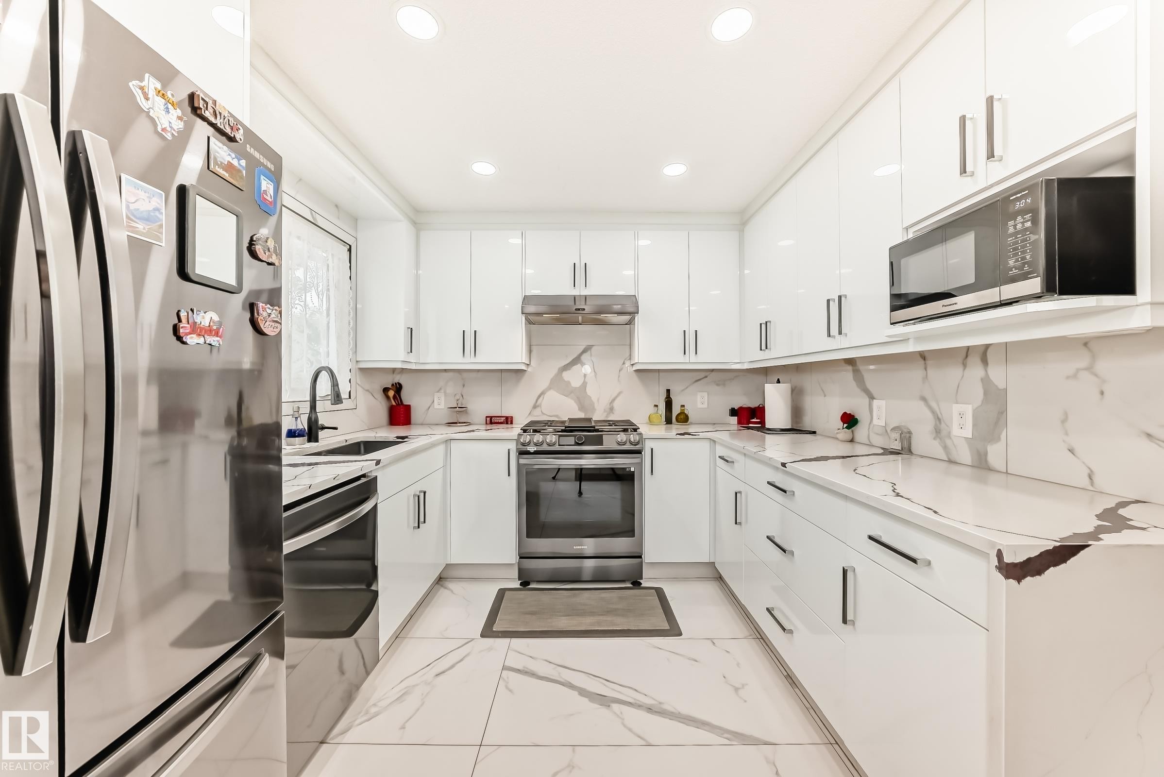 Modern kitchen featuring white high-gloss cabinetry with bar pull hardware, integrated stainless steel appliances, and a U-shaped countertop with a matching backsplash - 3843 47 Street Nw, Edmonton, AB - Indoor Photo Showing Kitchen With Upgraded Kitchen