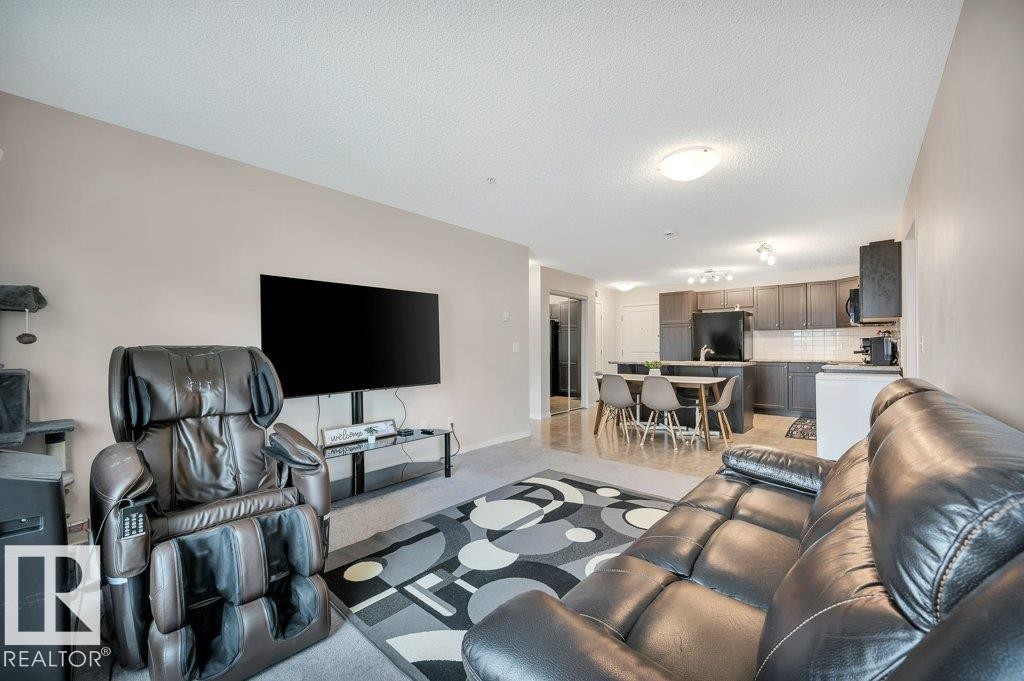 Open-concept living space featuring neutral wall tones, recessed lighting, and a kitchen with dark cabinetry, white subway tile backsplash, and a breakfast bar - 219 1820 Rutherford Road, Edmonton, AB