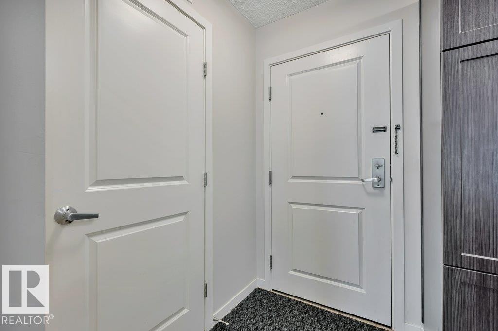 Entryway featuring a panel door with brushed nickel hardware, a secure entry door with a deadbolt and chain lock, and dark wood-finish cabinetry - 219 1820 Rutherford Road, Edmonton, AB